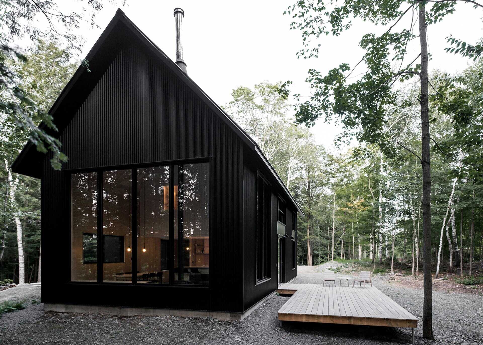 A striking black cottage tucked in a Quebec forest, blending modern design with traditional chalet forms for a moody, minimalist retreat.