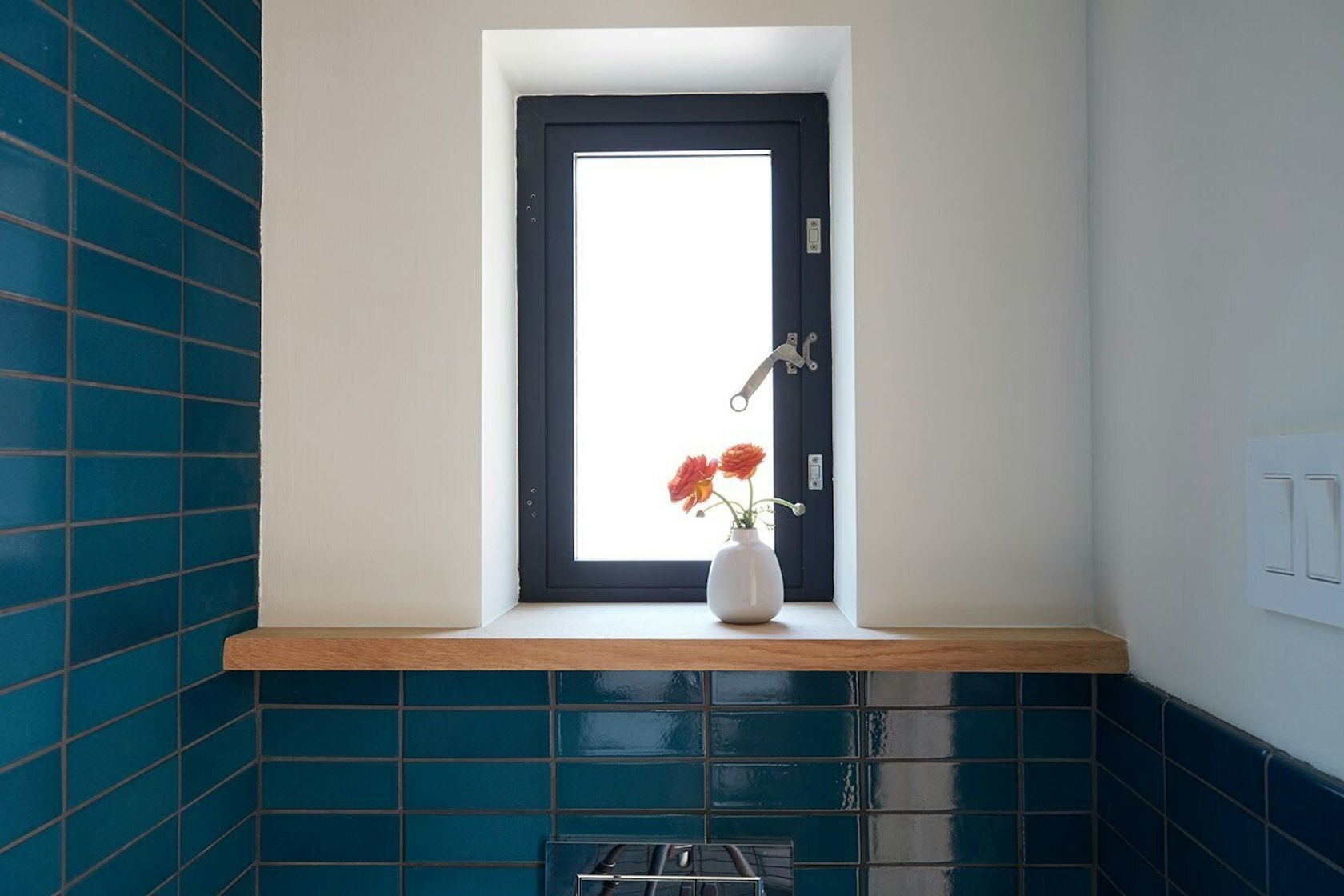 Tucked behind wooden shelving, this hidden powder room reveals bold blue tiles that bring unexpected energy to the refined studio.