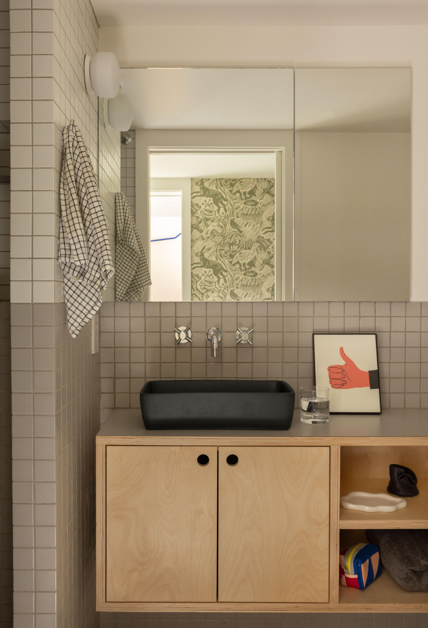 A modern bathroom with a floating wood vanity and square grey tiles.