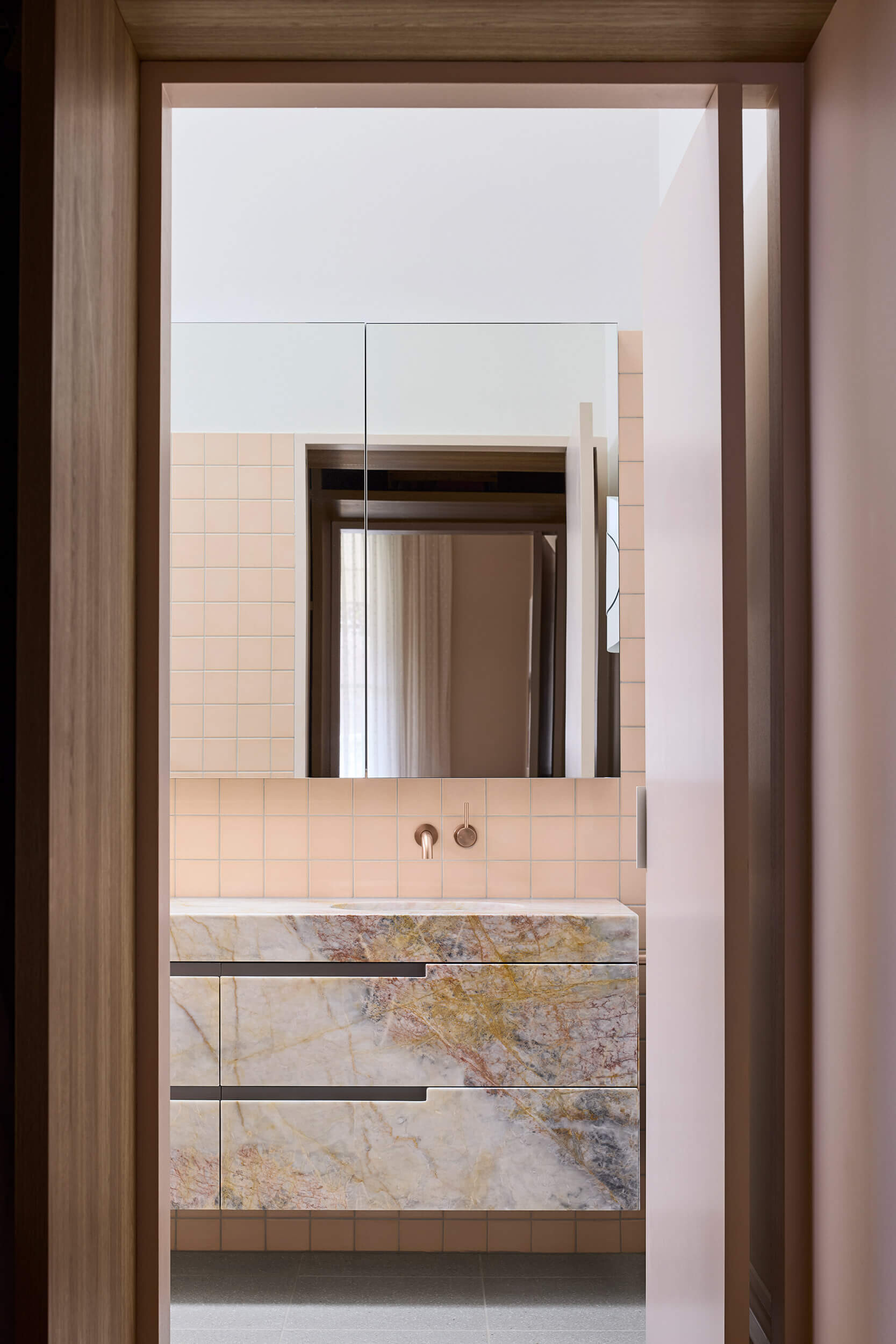 Australian marble with apricot and copper undertones carries through this ensuite bathroom, where color and texture build a sense of intimacy.