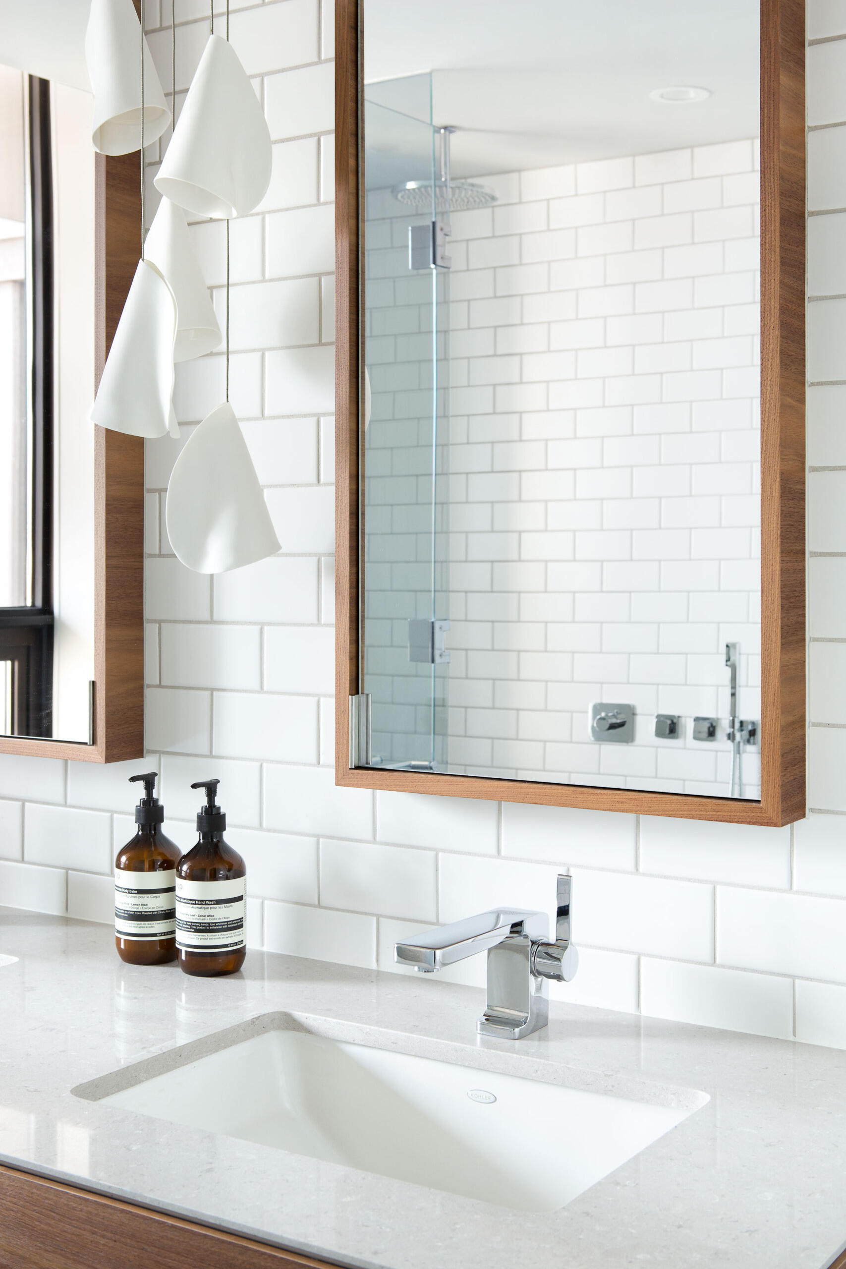 In the bathroom, white subway tiles climb the walls while dark grey geometric floor tiles anchor the space. A wood vanity with dual sinks mirrors the materials used below, giving the entire loft a sense of connection and flow.