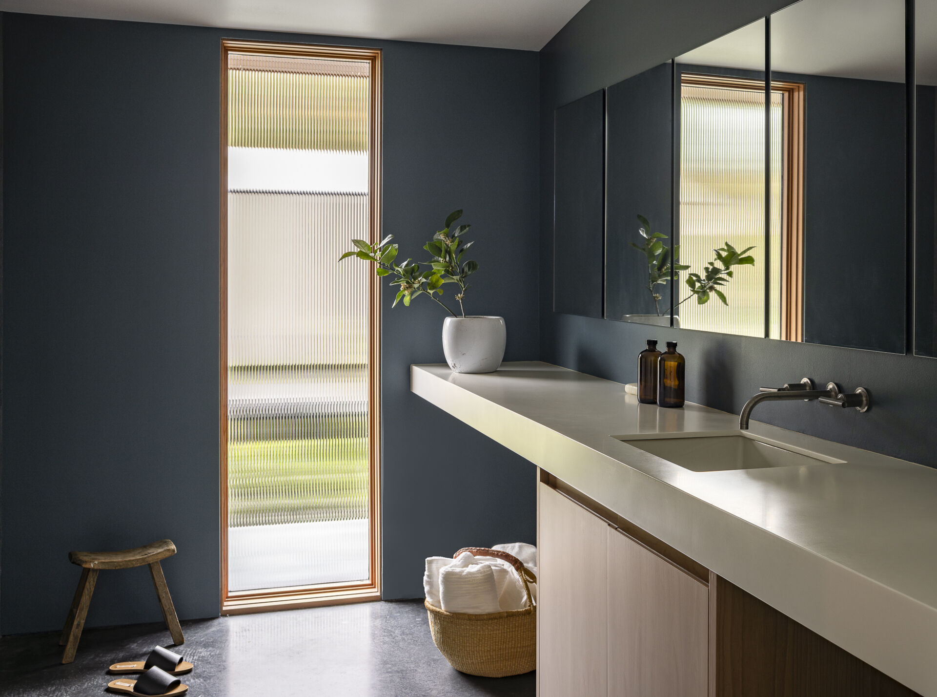 A modern bathroom with concrete floors, wide vanity, and vertical window.