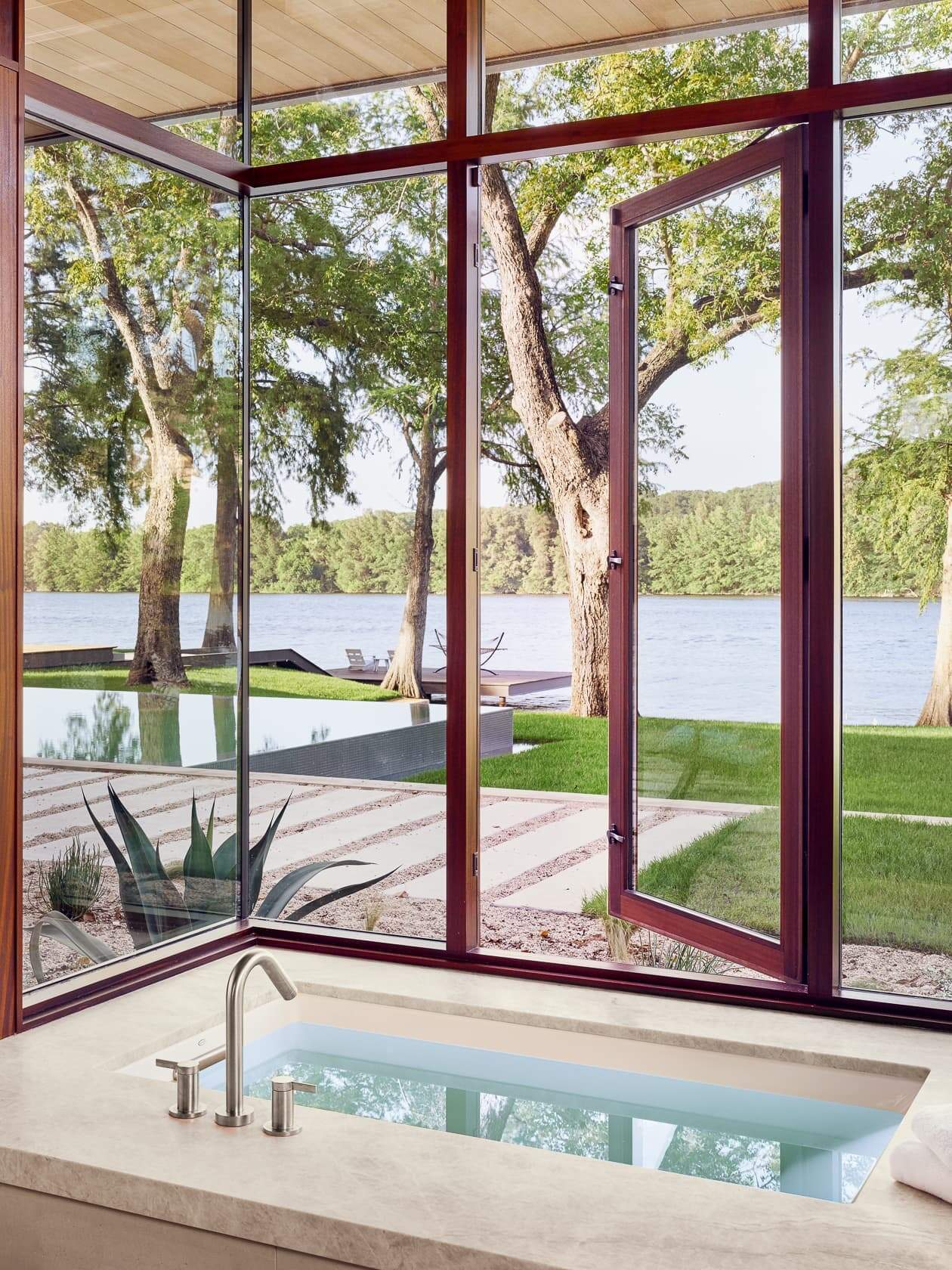 The master suite overlooks Lake Austin, with a soaking tub set beside wide windows that bathe the space in natural light.