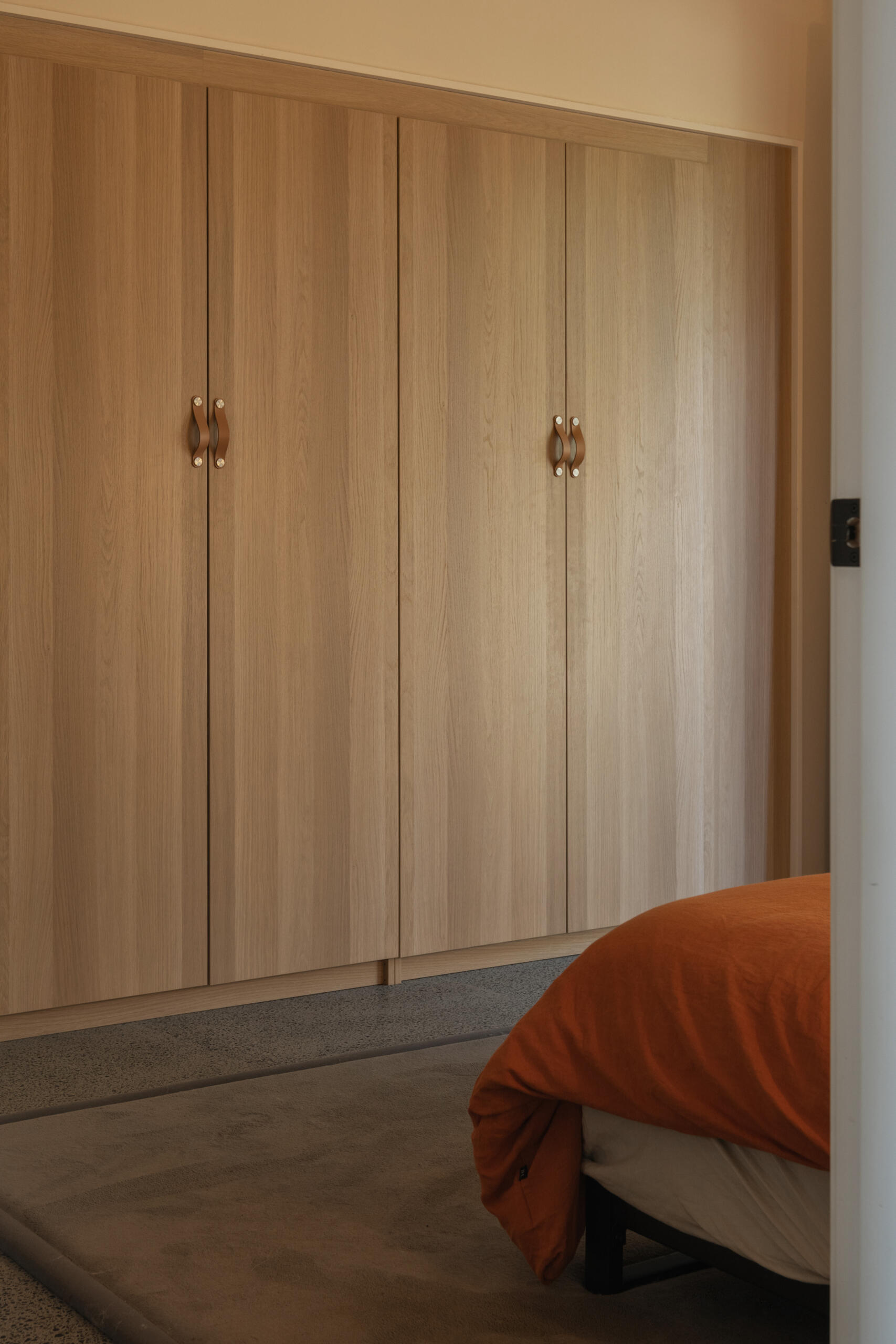 Soft, natural tones define the bedroom, where timber wardrobes with leather pulls create a seamless wall of storage.