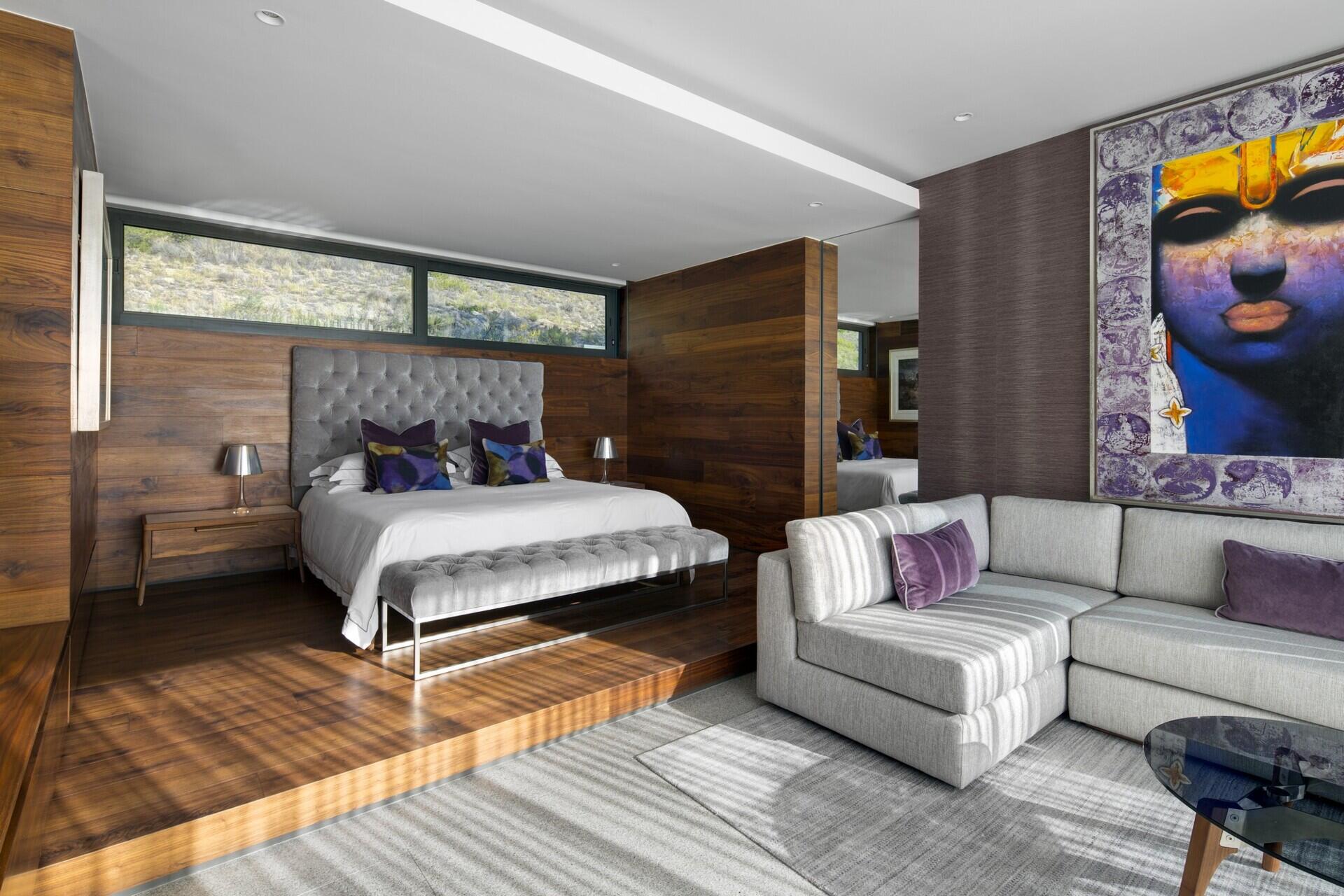 The master bedroom is a sanctuary with a raised wood platform bed, a grey lounge sofa, and large sliding glass walls that open onto a rooftop garden.