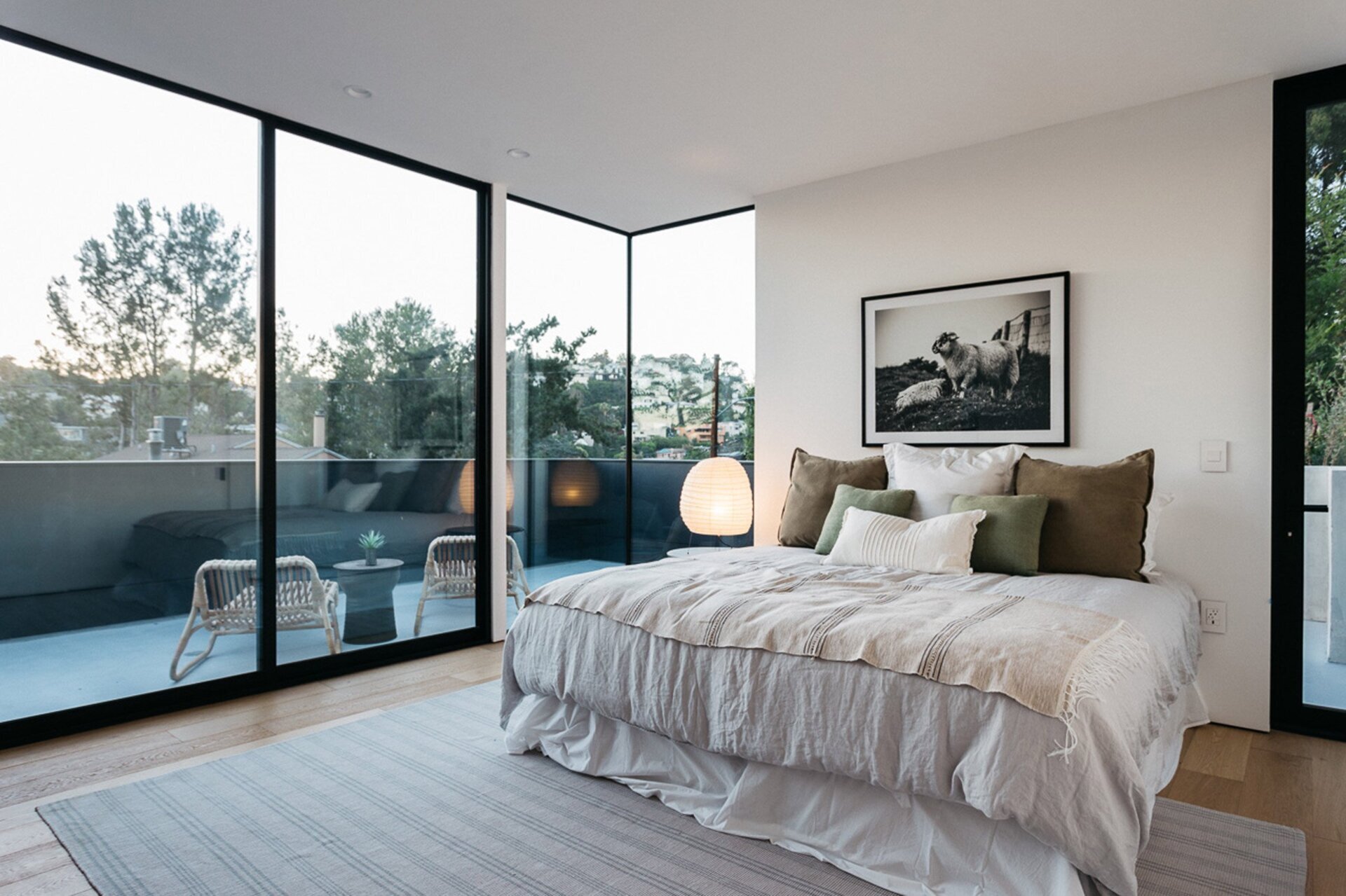 This primary bedroom feels both intimate and expansive. Floor-to-ceiling black-framed windows flood the space with natural light, while a matching door opens onto a private deck.
