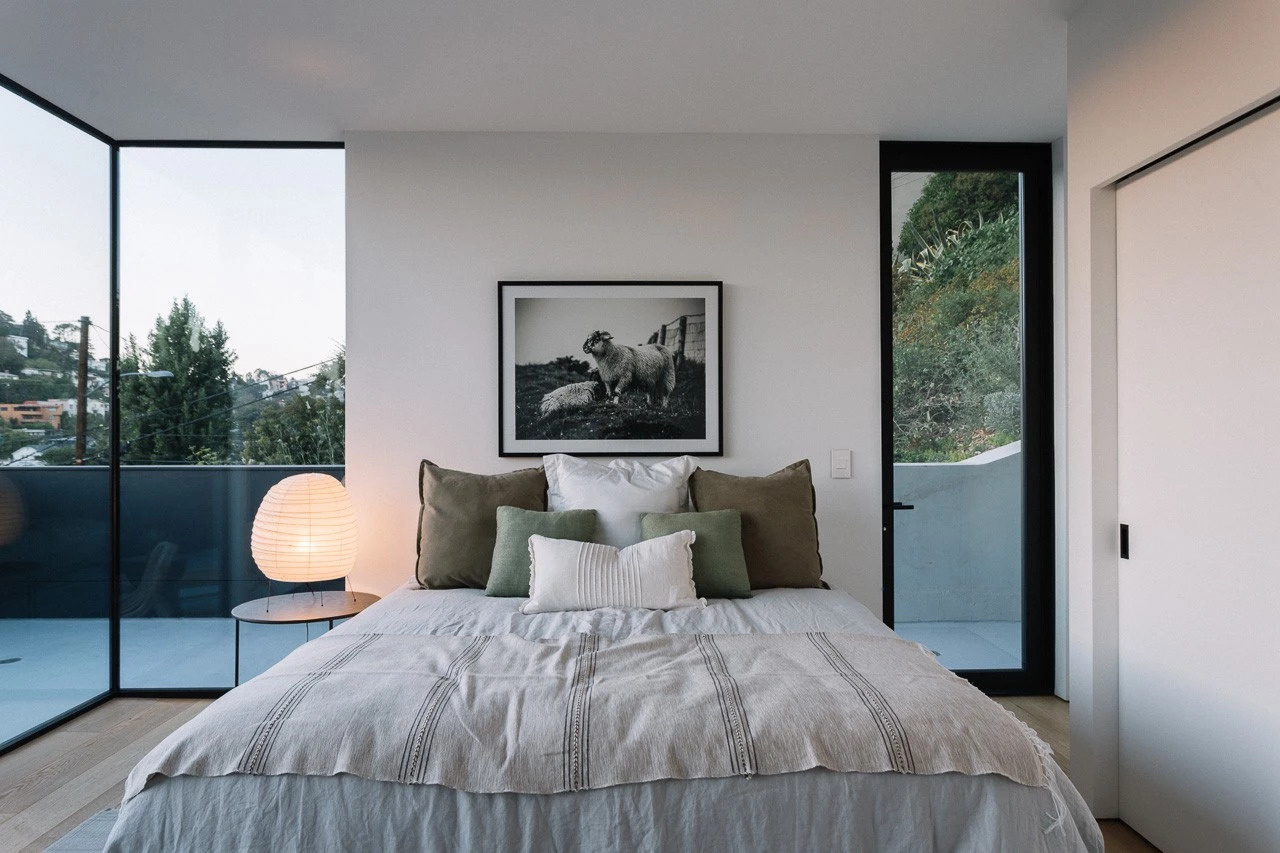 This primary bedroom feels both intimate and expansive. Floor-to-ceiling black-framed windows flood the space with natural light, while a matching door opens onto a private deck.