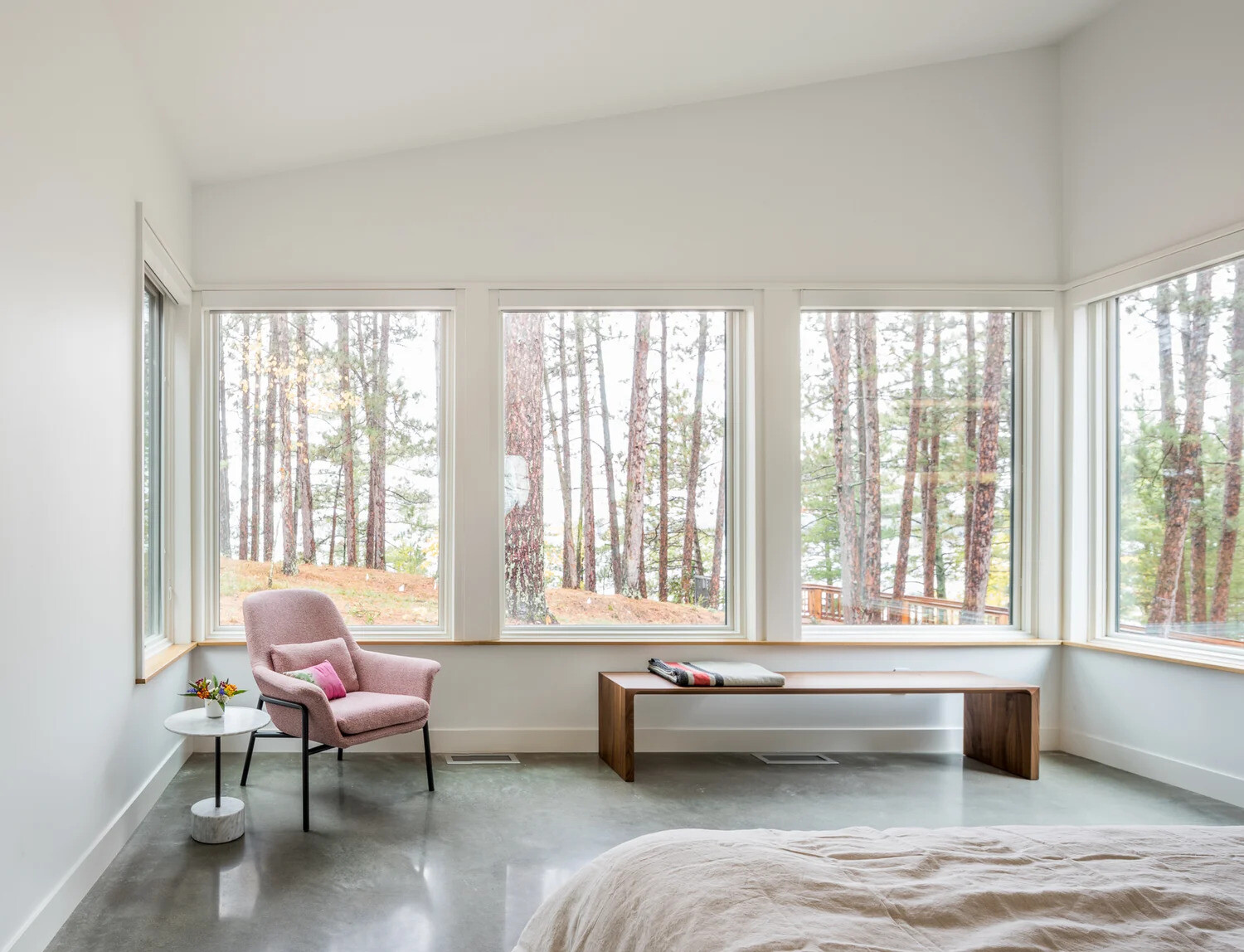 In the bedroom, windows wrap around one end of the room, creating a natural frame for the surrounding forest.