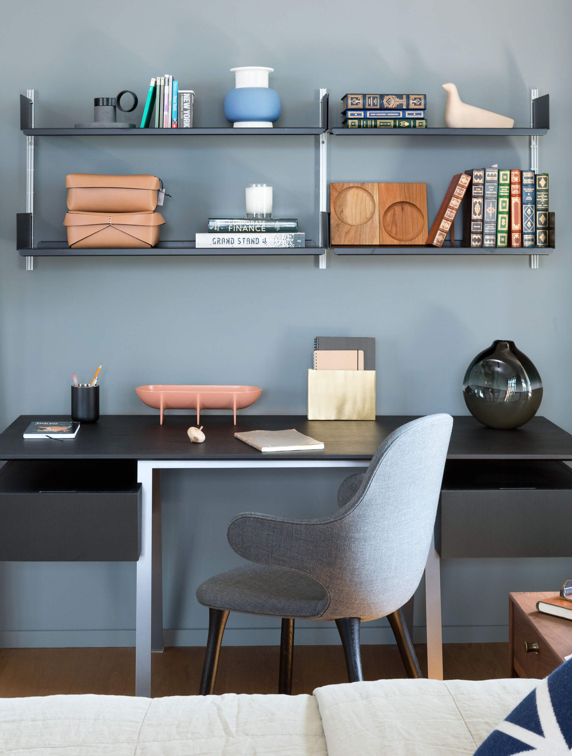 A simple wood bed frame and side tables feel tactile and grounded, while a small workspace with open shelving tucks neatly beside the window. Every surface serves a purpose without overwhelming the calm.