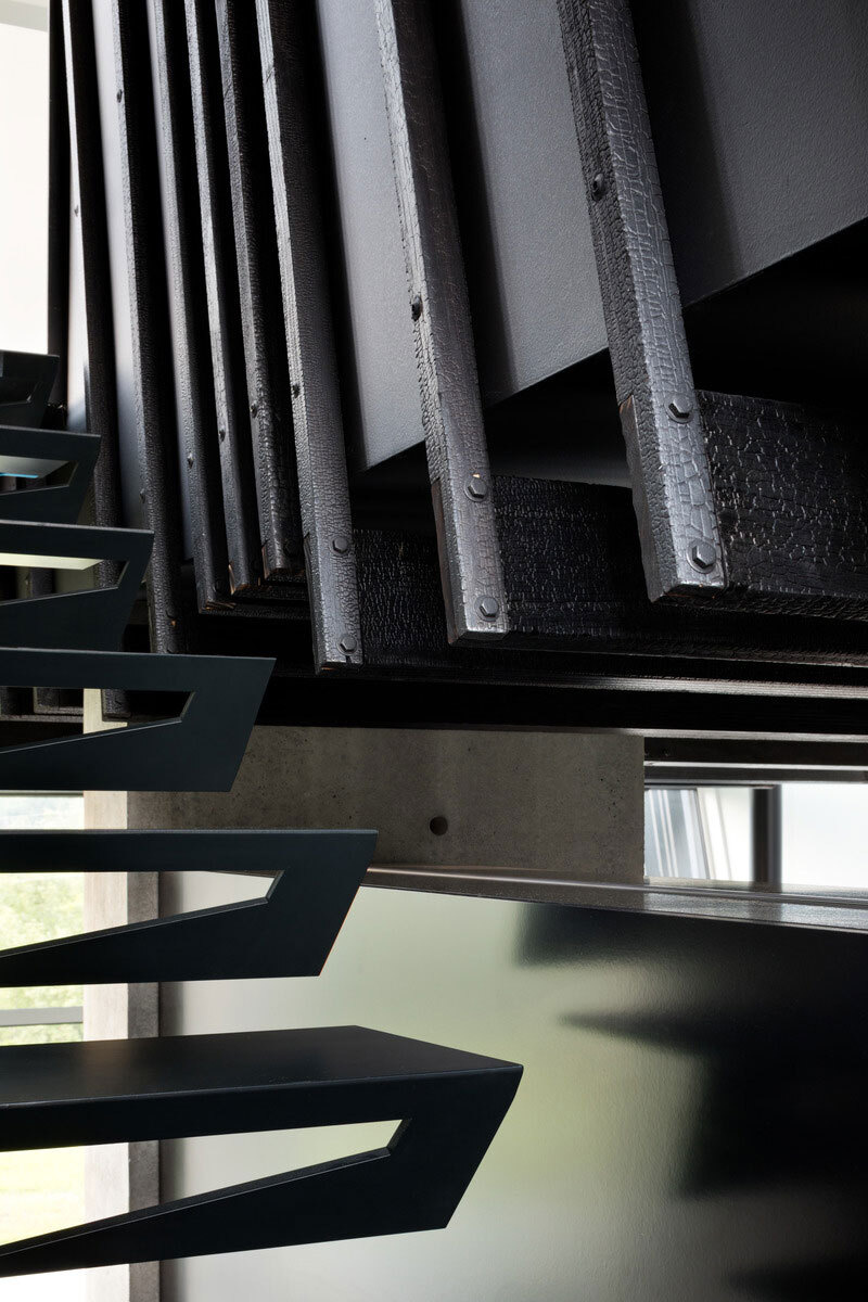 A black sculptural staircase leads to calm, light-filled bedrooms where Shou Sugi Ban details continue the home’s cohesive design.