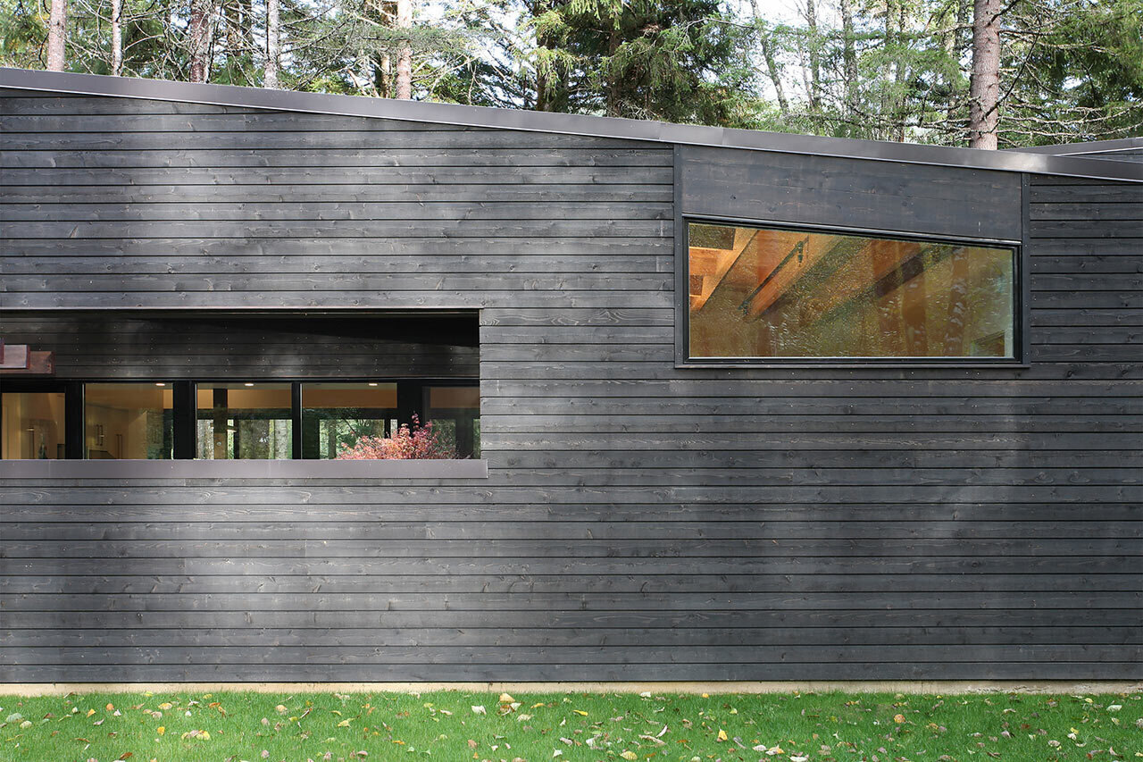 A sleek, single-story house by Robert Hutchison Architecture, wrapped in blackened cedar and nestled quietly among the evergreens near Mount Rainier.