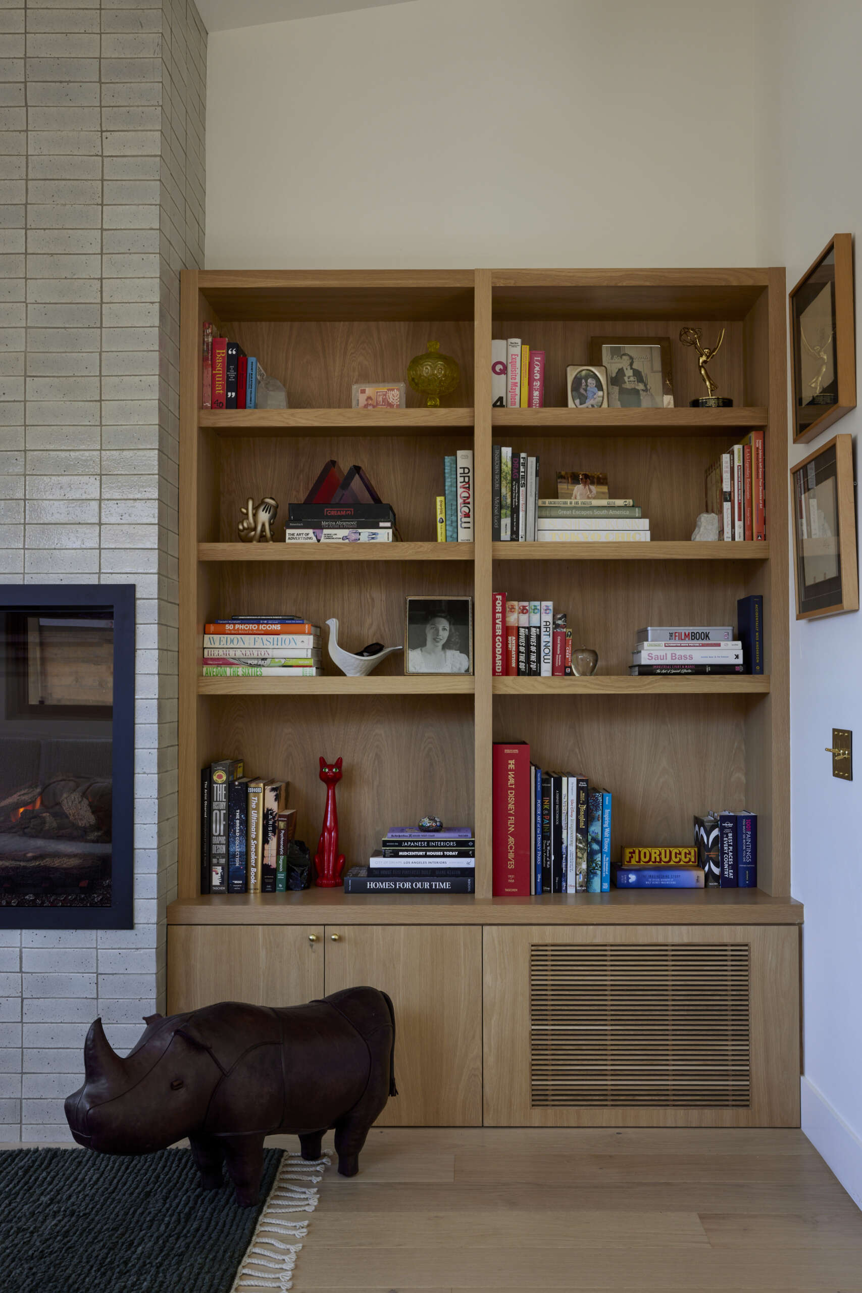 Built-in sofas, end tables, and storage make the narrow living room feel purposeful, while an electric fireplace and custom wood HVAC grille bring both style and comfort.