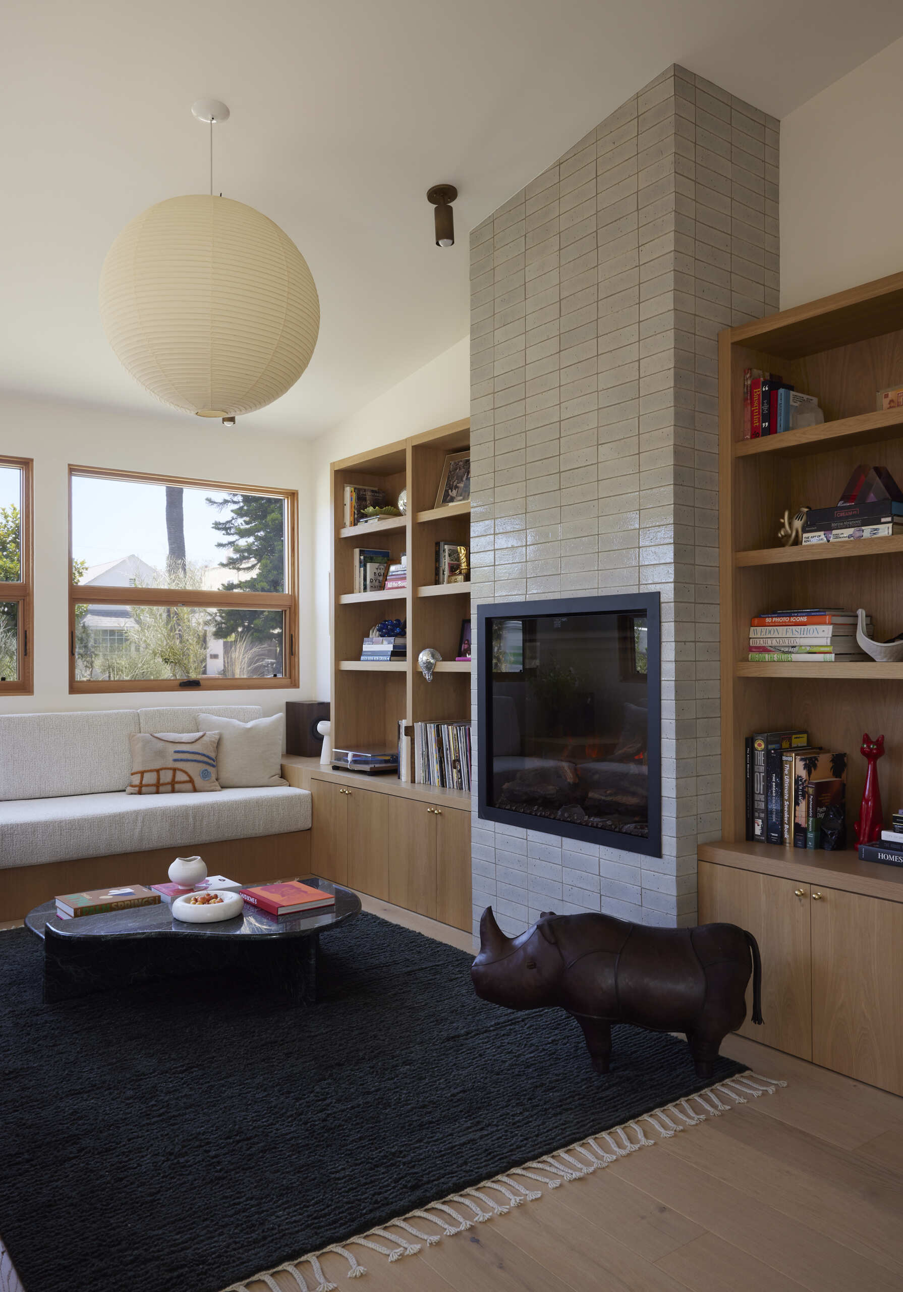Built-in sofas, end tables, and storage make the narrow living room feel purposeful, while an electric fireplace and custom wood HVAC grille bring both style and comfort.
