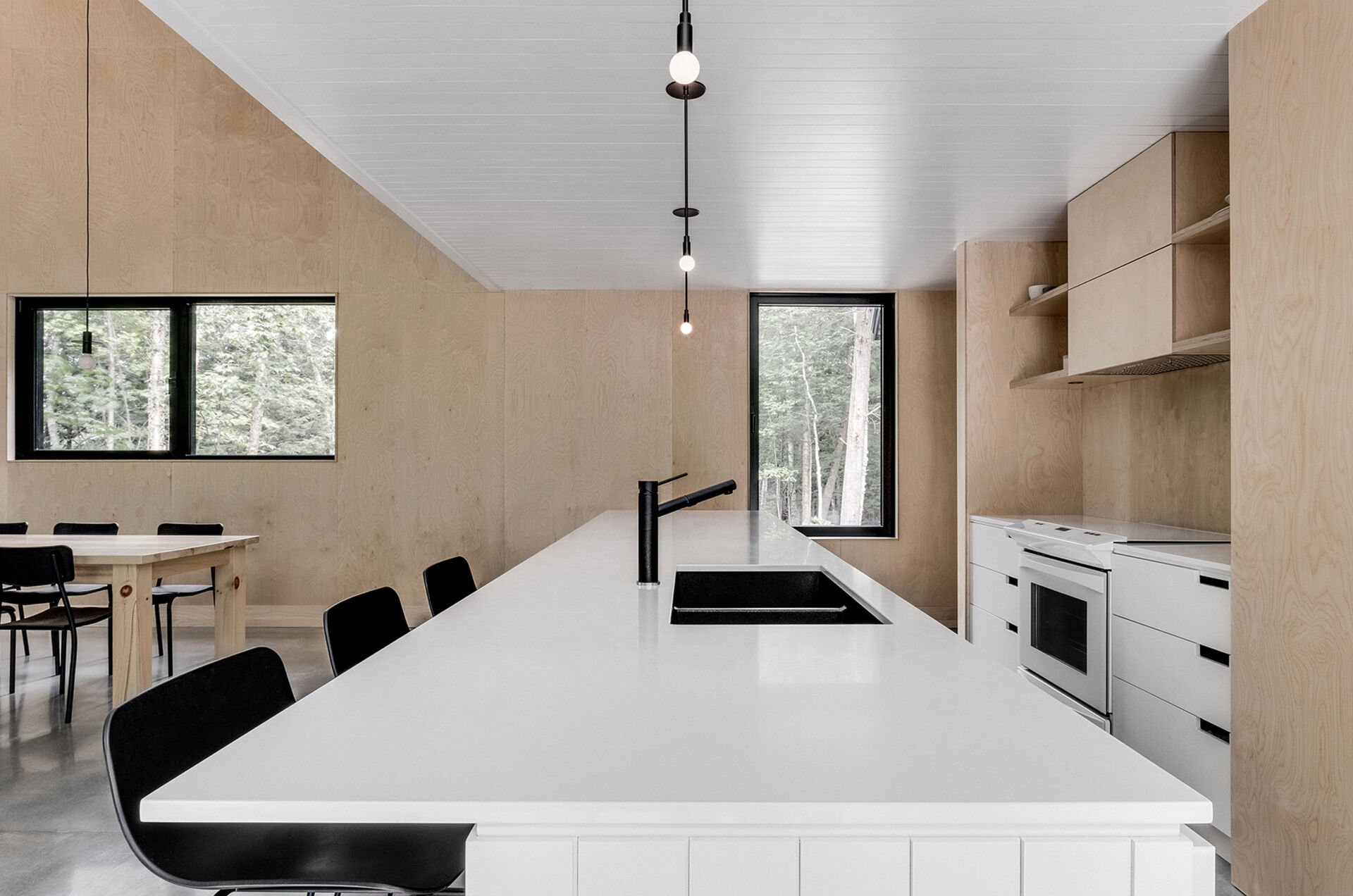 A bright, understated kitchen with polished concrete floors and light wood finishes connects seamlessly to the outdoors through glass doors.