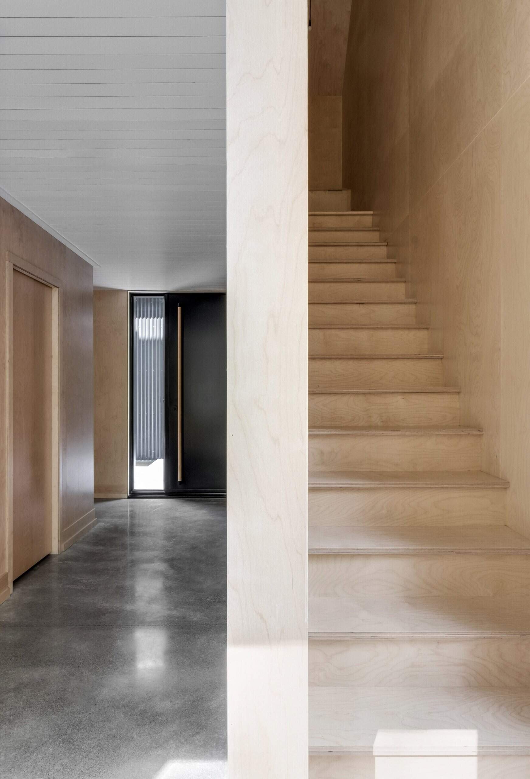 A wooden staircase leads to tranquil bedrooms above, where light and landscape define the calm, airy mood of the cottage.