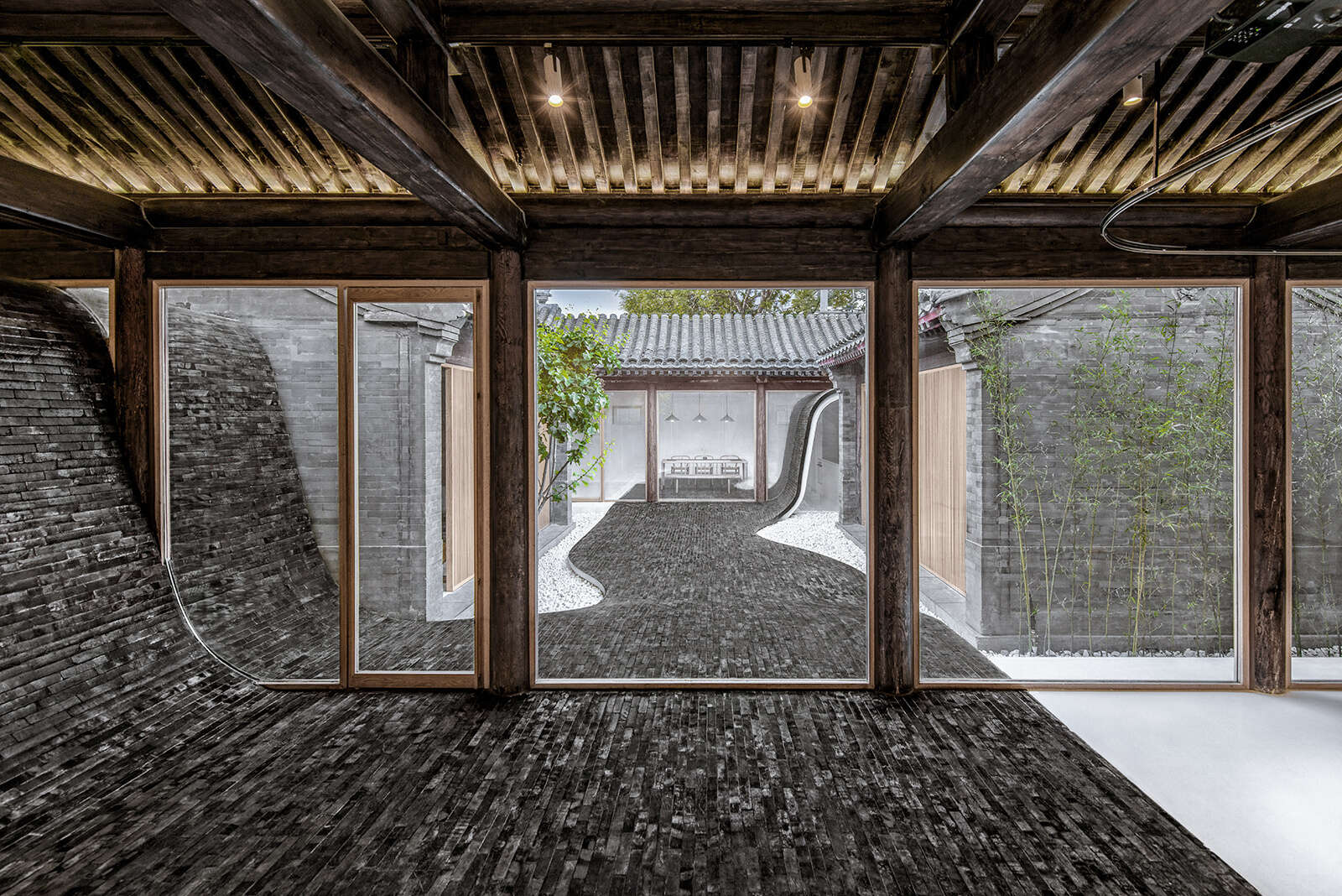 Dark tiles curve from roof to courtyard, connecting indoor and outdoor spaces and creating a dynamic walking path that comes alive at night.