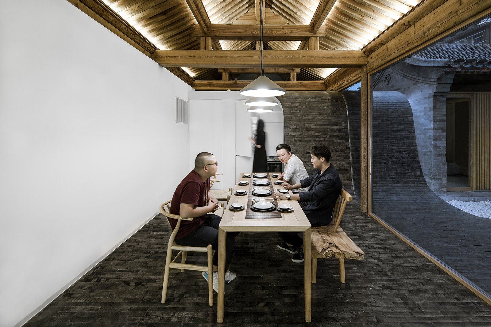 A long wood table under three pendant lights anchors the dining space, seamlessly linking it to the courtyard outside.