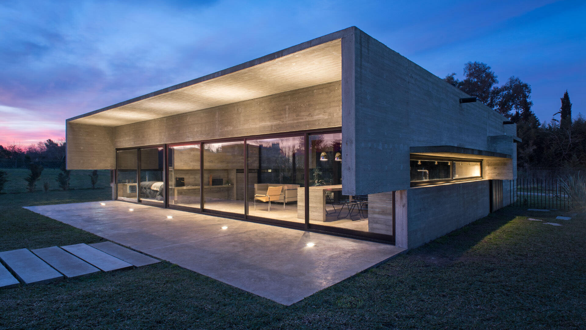 A modern concrete home in Buenos Aires with pools at both ends and a glowing overhang that transforms at night.