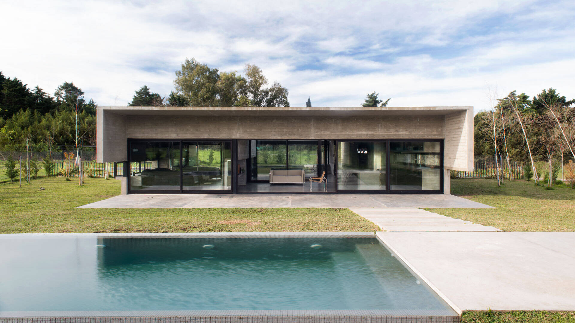 A modern concrete home in Buenos Aires with pools at both ends and a glowing overhang that transforms at night.