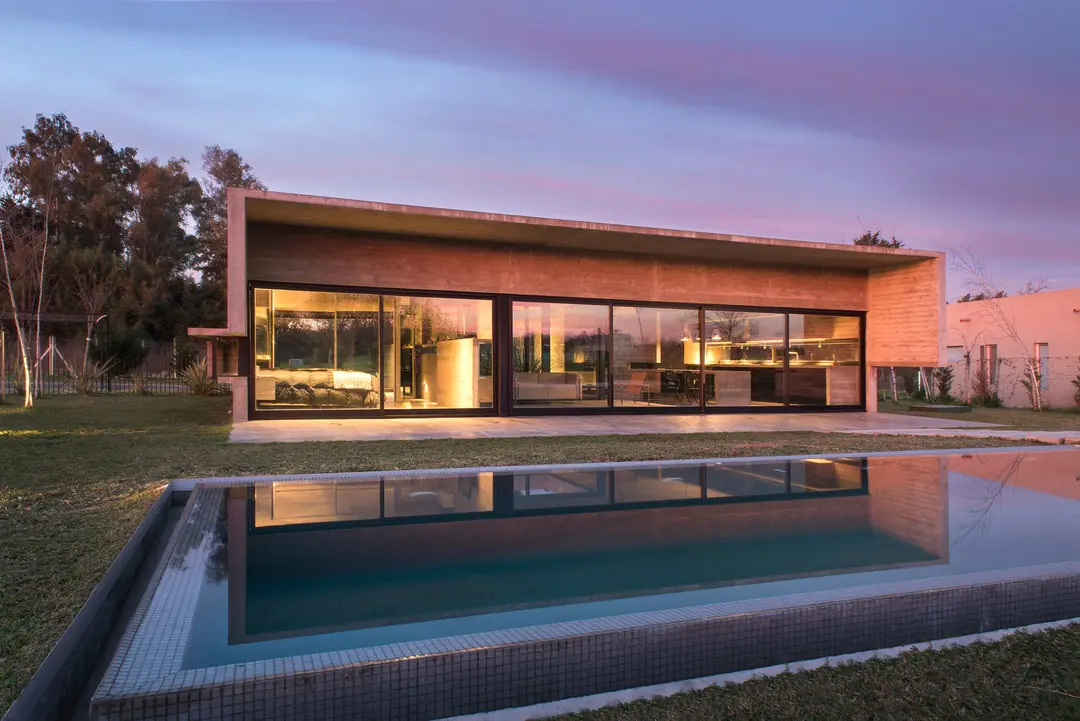 A modern concrete home in Buenos Aires with pools at both ends and a glowing overhang that transforms at night.
