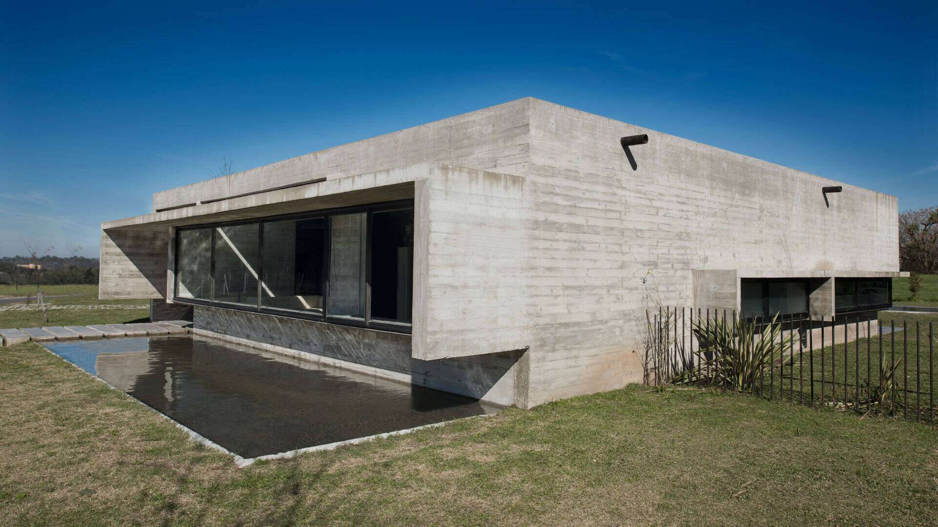 A modern concrete home in Buenos Aires with pools at both ends and a glowing overhang that transforms at night.