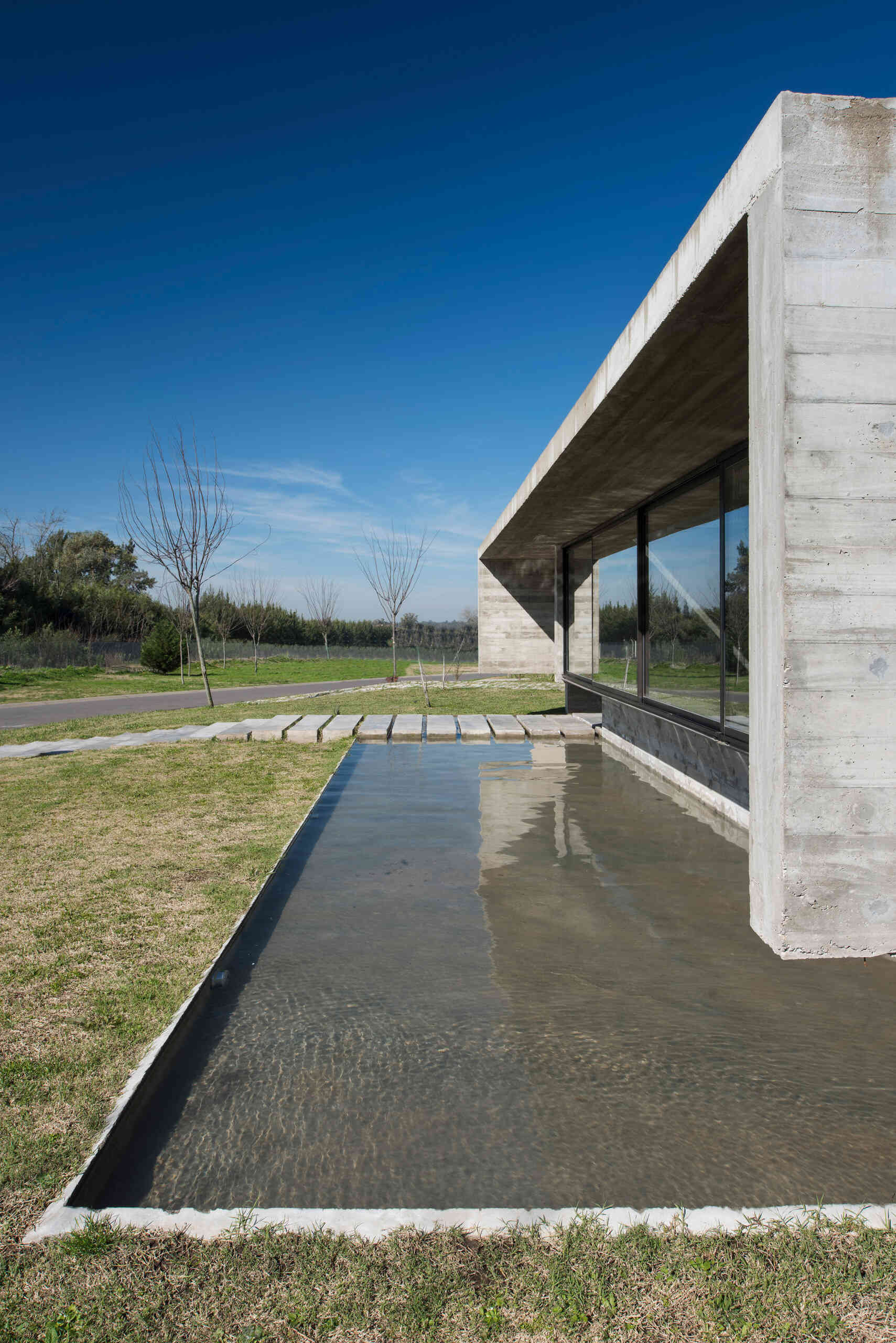 A modern concrete home in Buenos Aires with pools at both ends and a glowing overhang that transforms at night.