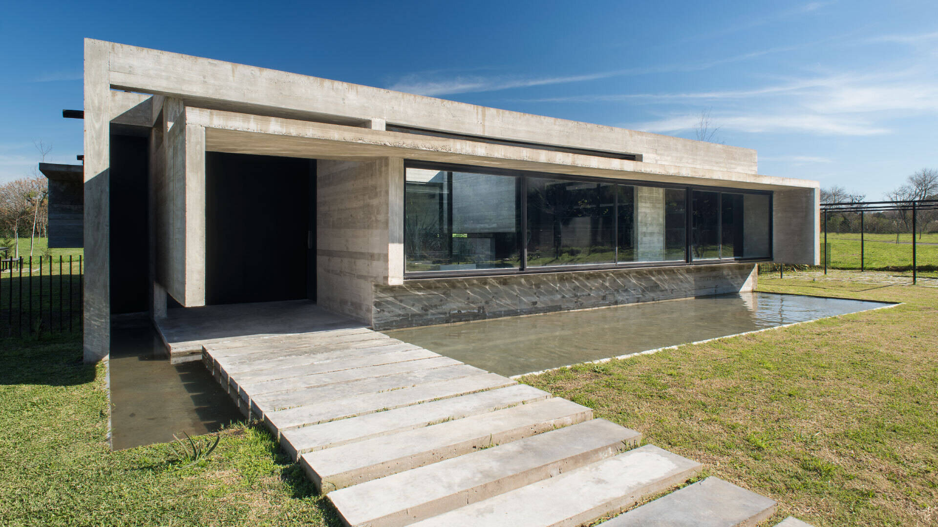 A modern concrete home in Buenos Aires with pools at both ends and a glowing overhang that transforms at night.