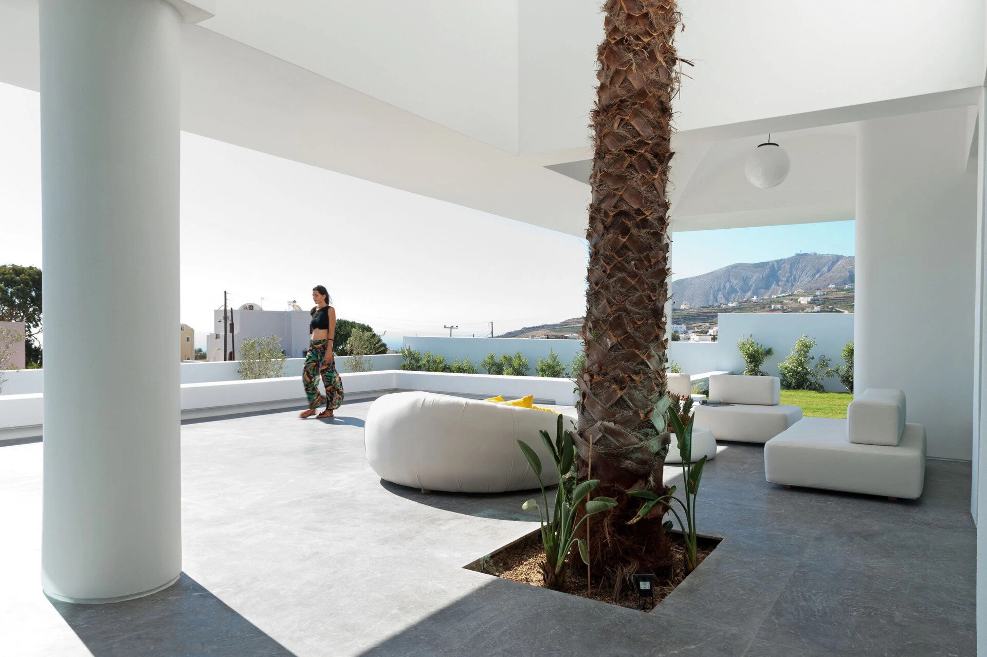 A tall palm tree becomes the centerpiece of this Santorini summer house, uniting indoor and outdoor spaces in one luminous, breezy living area.