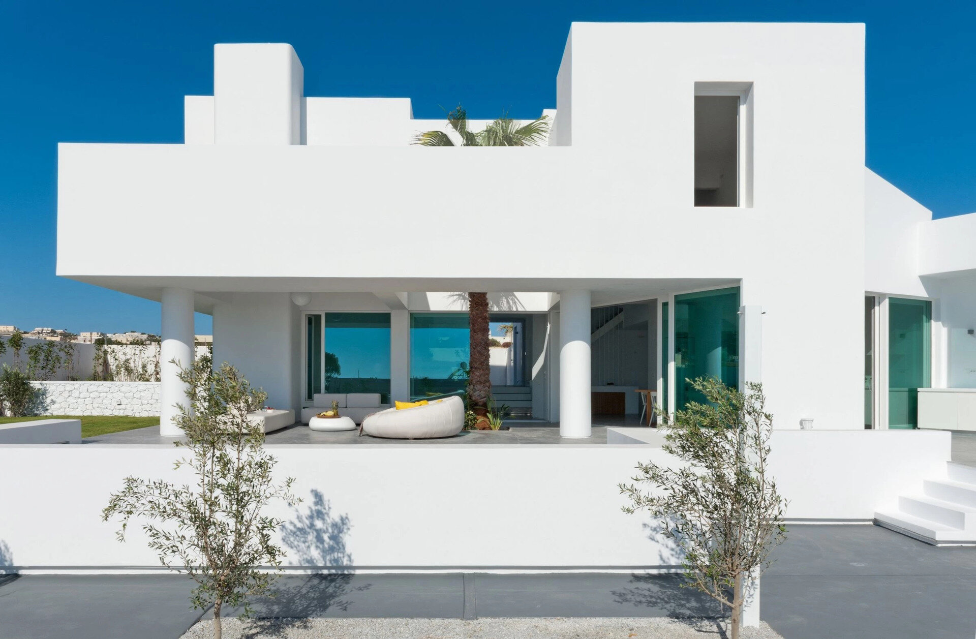 A tall palm tree becomes the centerpiece of this Santorini summer house, uniting indoor and outdoor spaces in one luminous, breezy living area.