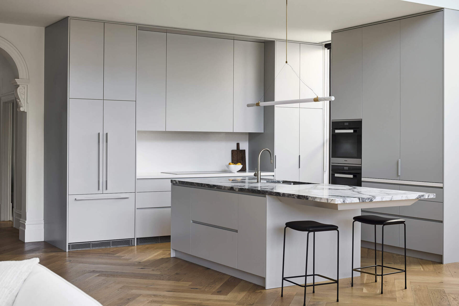 This kitchen centers on a cantilevered stone island that serves as both sculptural statement and family gathering point. Suspended lighting in brass and marble continues the refined aesthetic. Hidden appliances maintain a sense of calm order, reinforcing the balance of function and beauty.