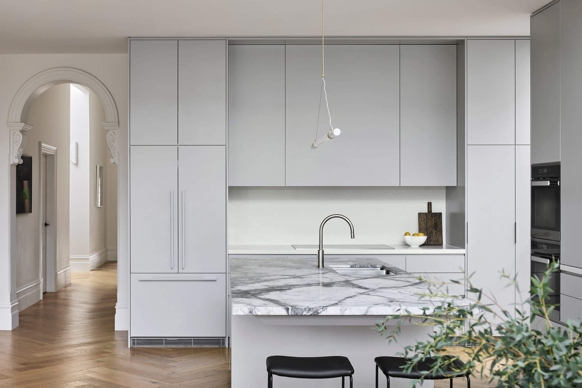 This kitchen centers on a cantilevered stone island that serves as both sculptural statement and family gathering point. Suspended lighting in brass and marble continues the refined aesthetic. Hidden appliances maintain a sense of calm order, reinforcing the balance of function and beauty.