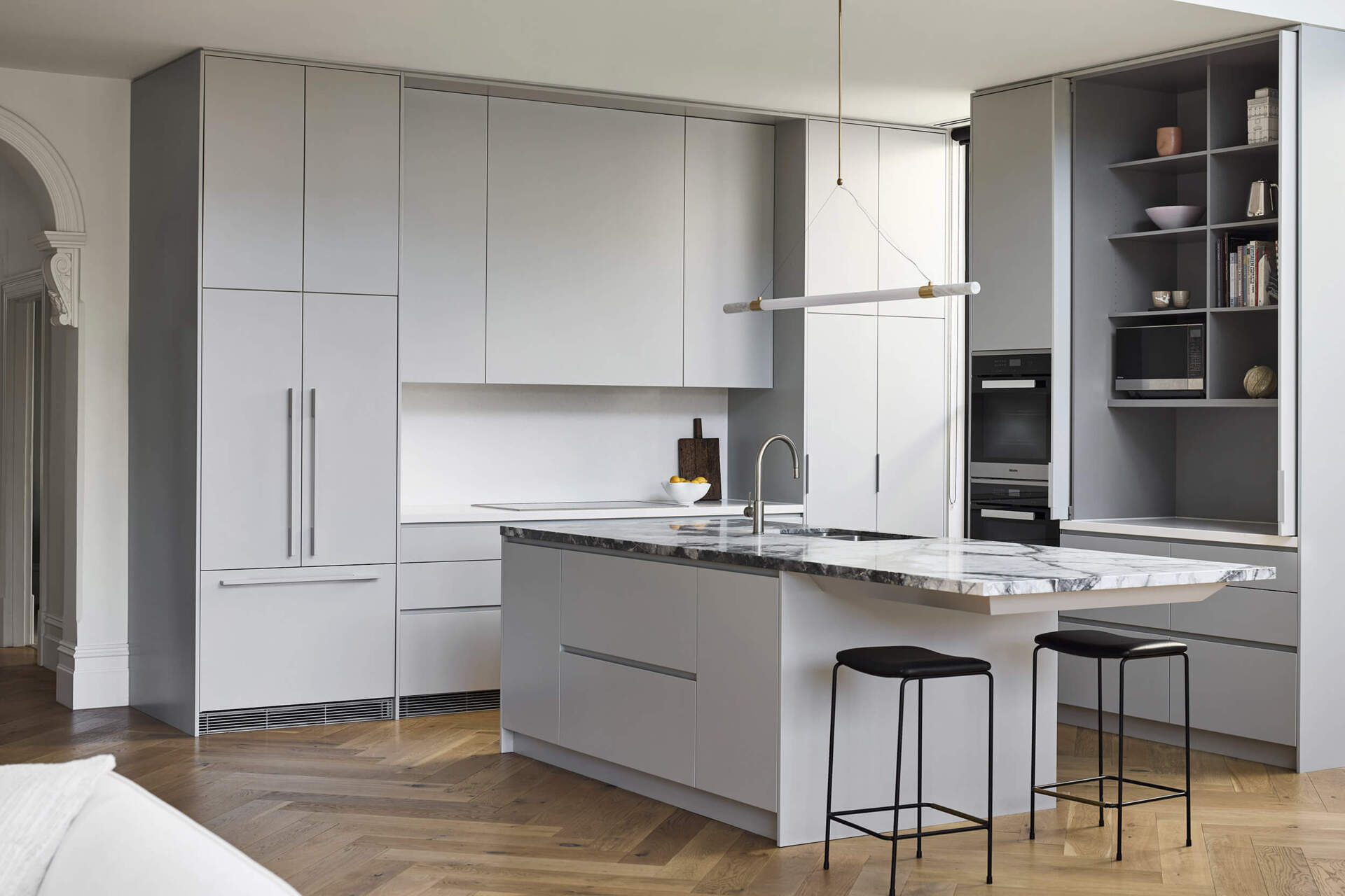 This kitchen centers on a cantilevered stone island that serves as both sculptural statement and family gathering point. Suspended lighting in brass and marble continues the refined aesthetic. Hidden appliances maintain a sense of calm order, reinforcing the balance of function and beauty.