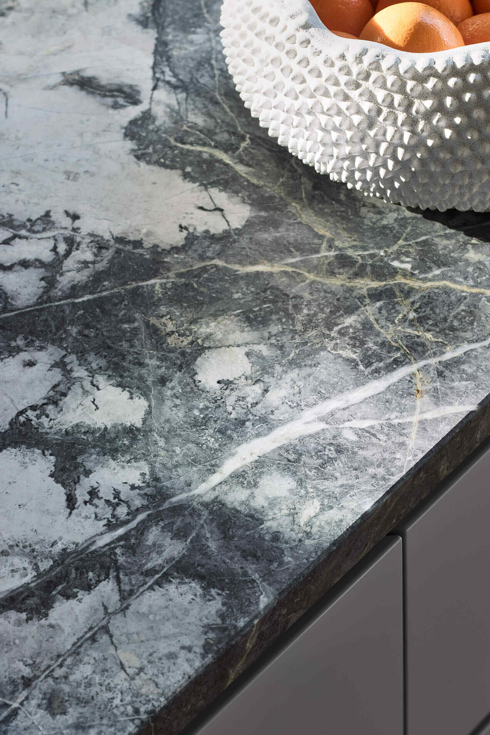 This kitchen centers on a cantilevered stone island that serves as both sculptural statement and family gathering point. Suspended lighting in brass and marble continues the refined aesthetic. Hidden appliances maintain a sense of calm order, reinforcing the balance of function and beauty.