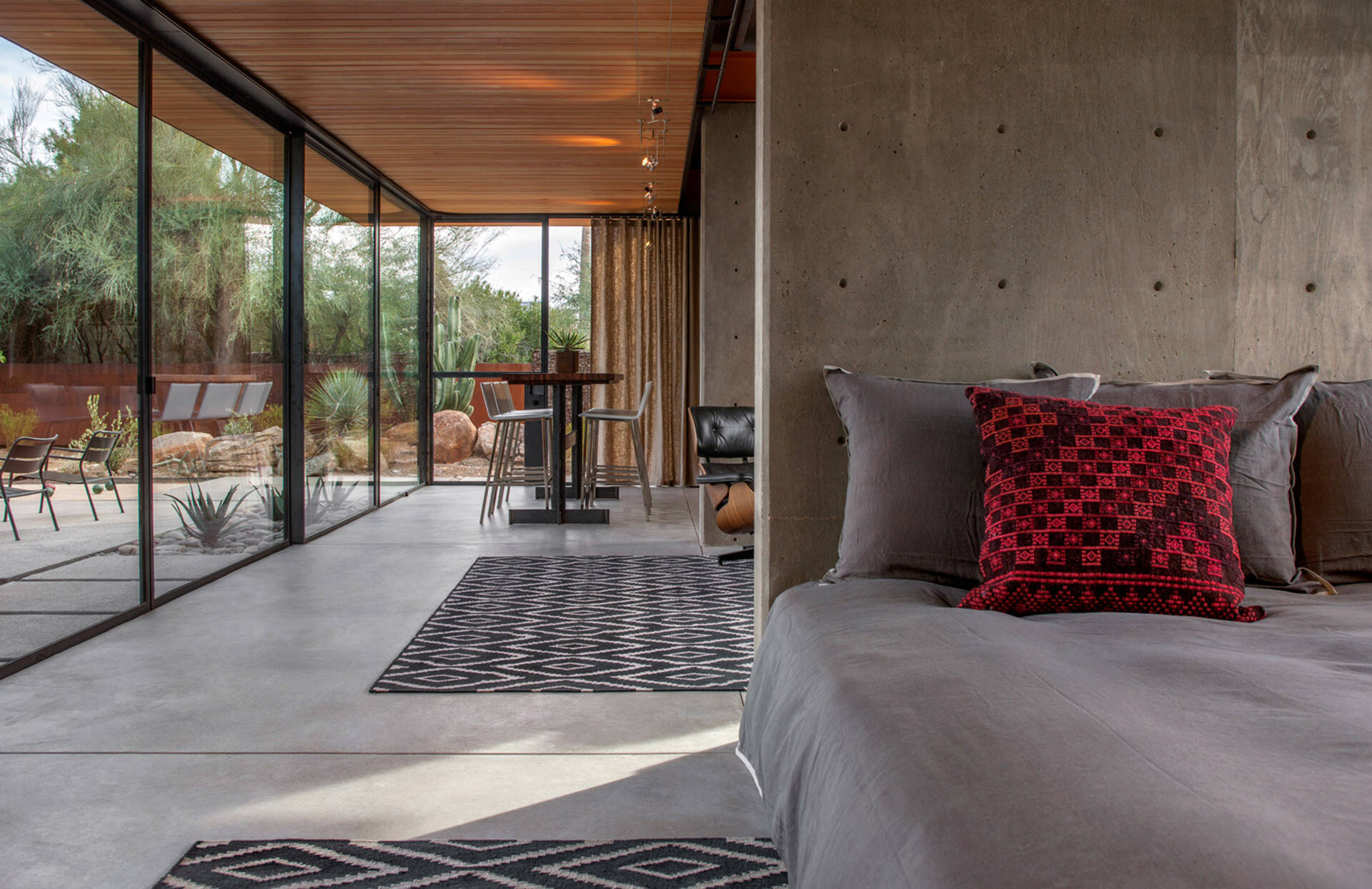 Concrete, wood, and touches of red define the bedroom’s minimalist palette, where a solid concrete wall doubles as a headboard.