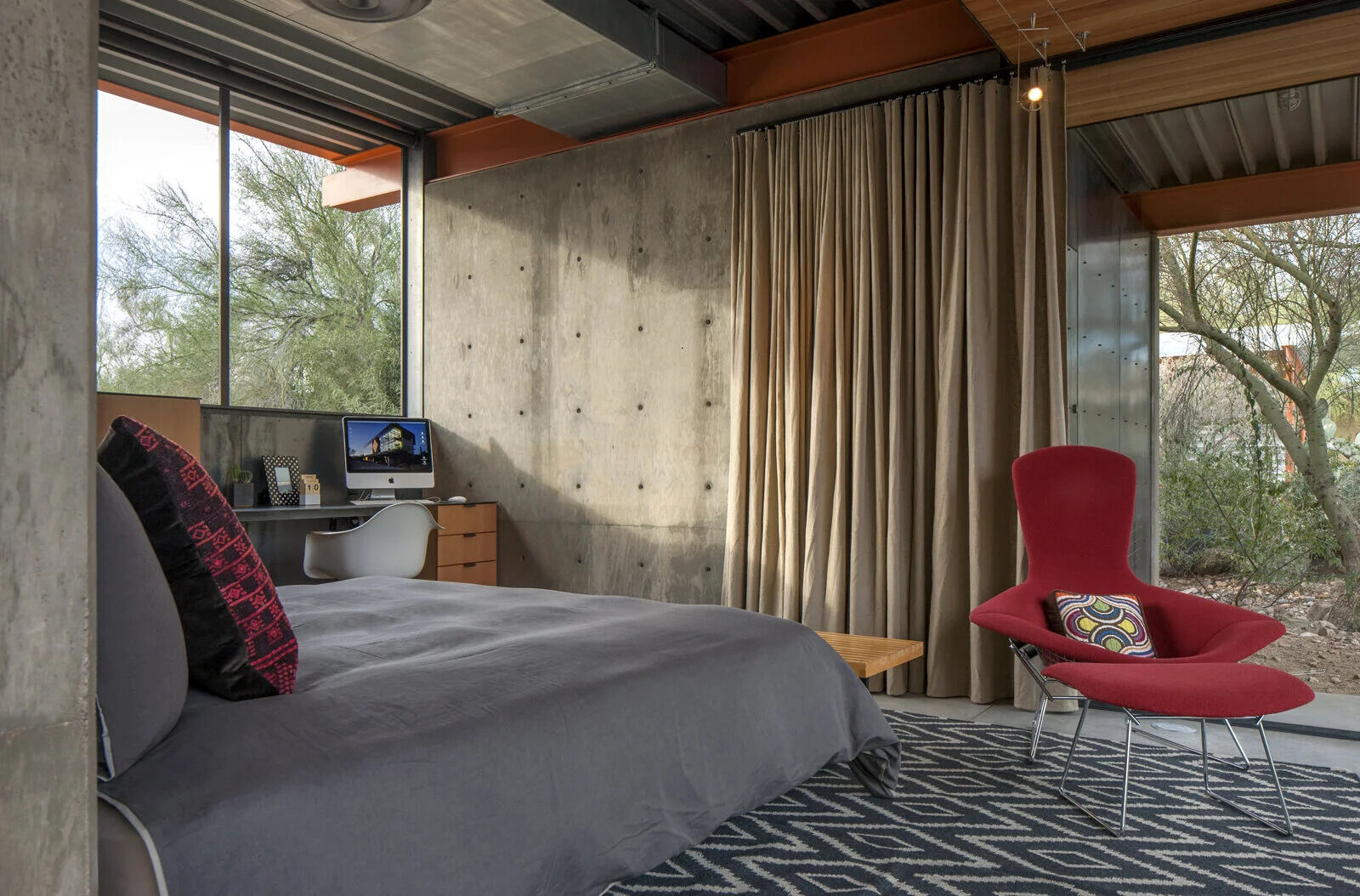 Concrete, wood, and touches of red define the bedroom’s minimalist palette, where a solid concrete wall doubles as a headboard.