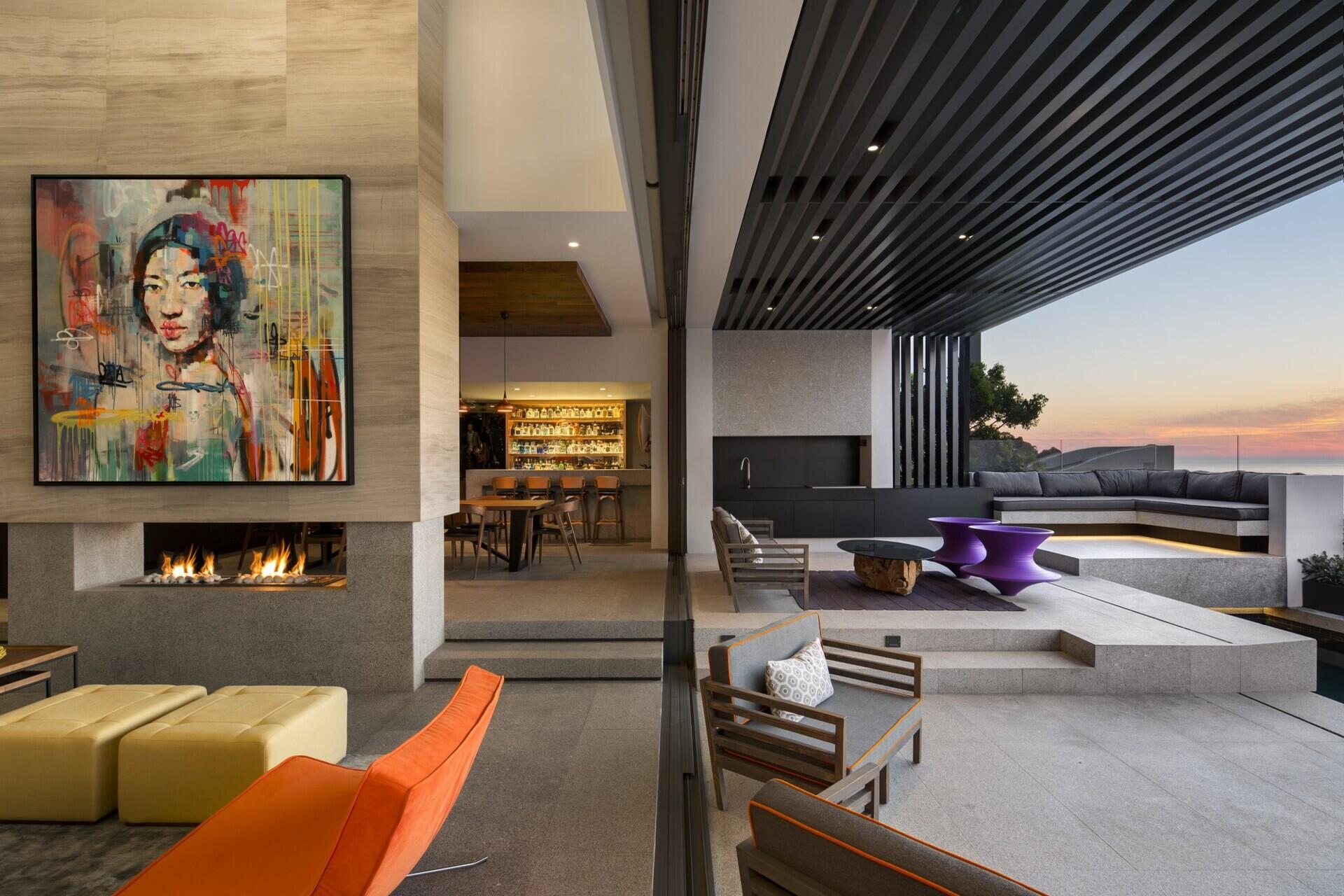 A vibrant, contemporary living room with a double-sided fireplace opens to a covered outdoor lounge and plunge pool.