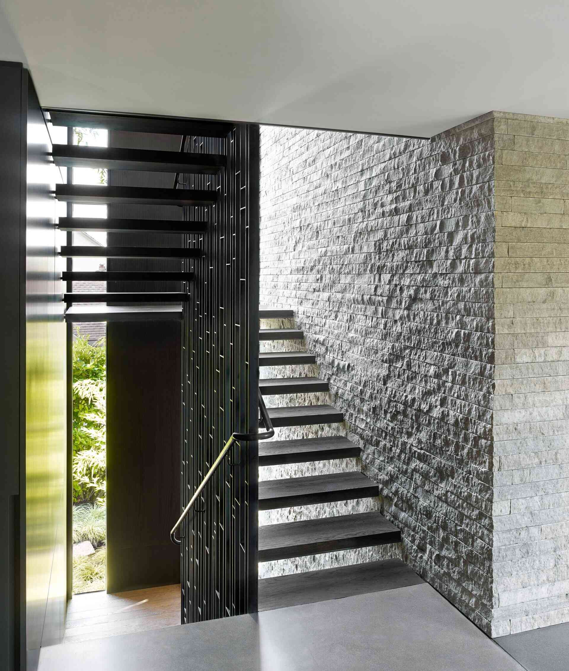 The stone wall from the living room continues along the staircase, creating a visual link between the levels. A light steel stair column was engineered to carry the structural load, doing away with heavy stringers and giving the stairs a floating effect.