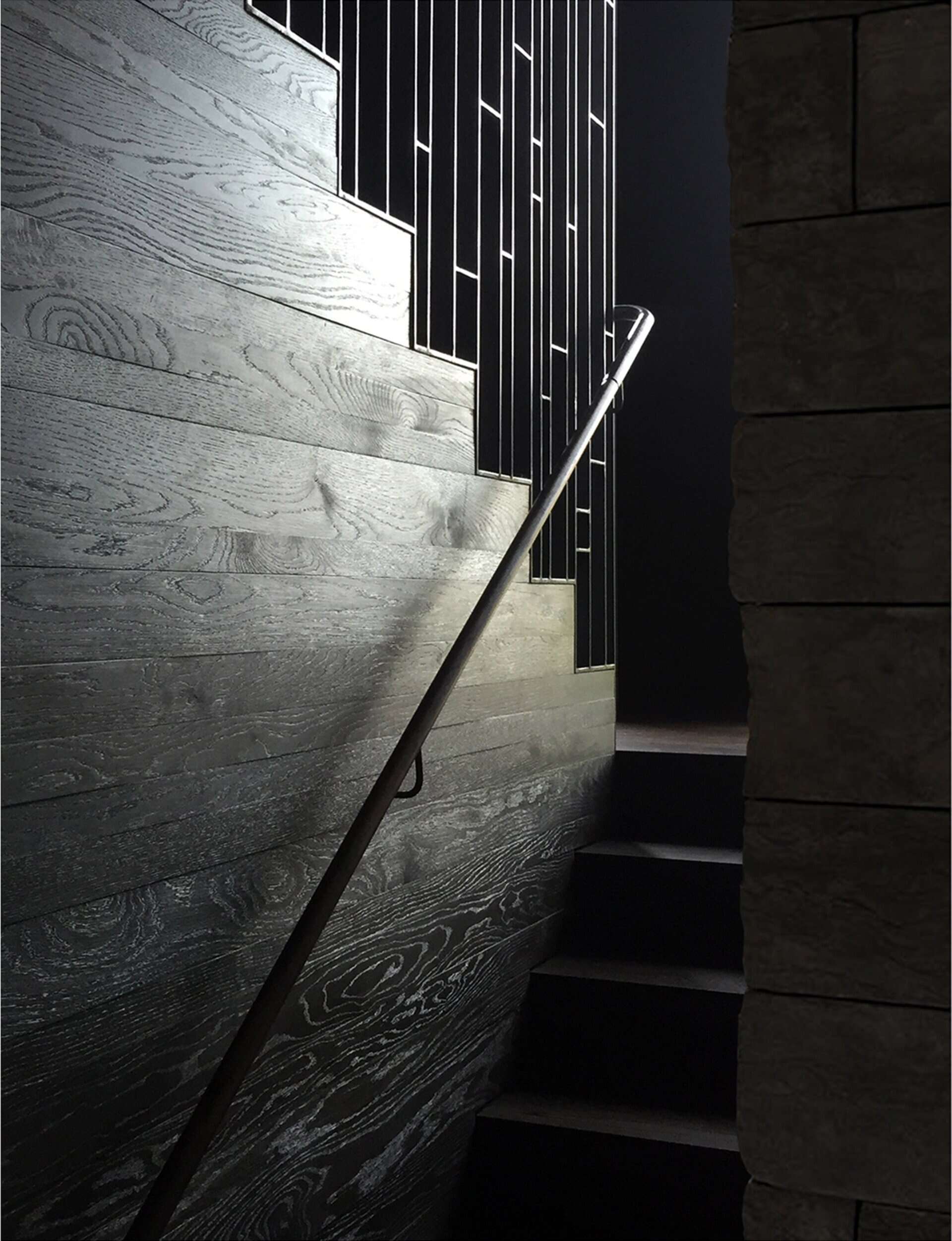 The stone wall from the living room continues along the staircase, creating a visual link between the levels. A light steel stair column was engineered to carry the structural load, doing away with heavy stringers and giving the stairs a floating effect.