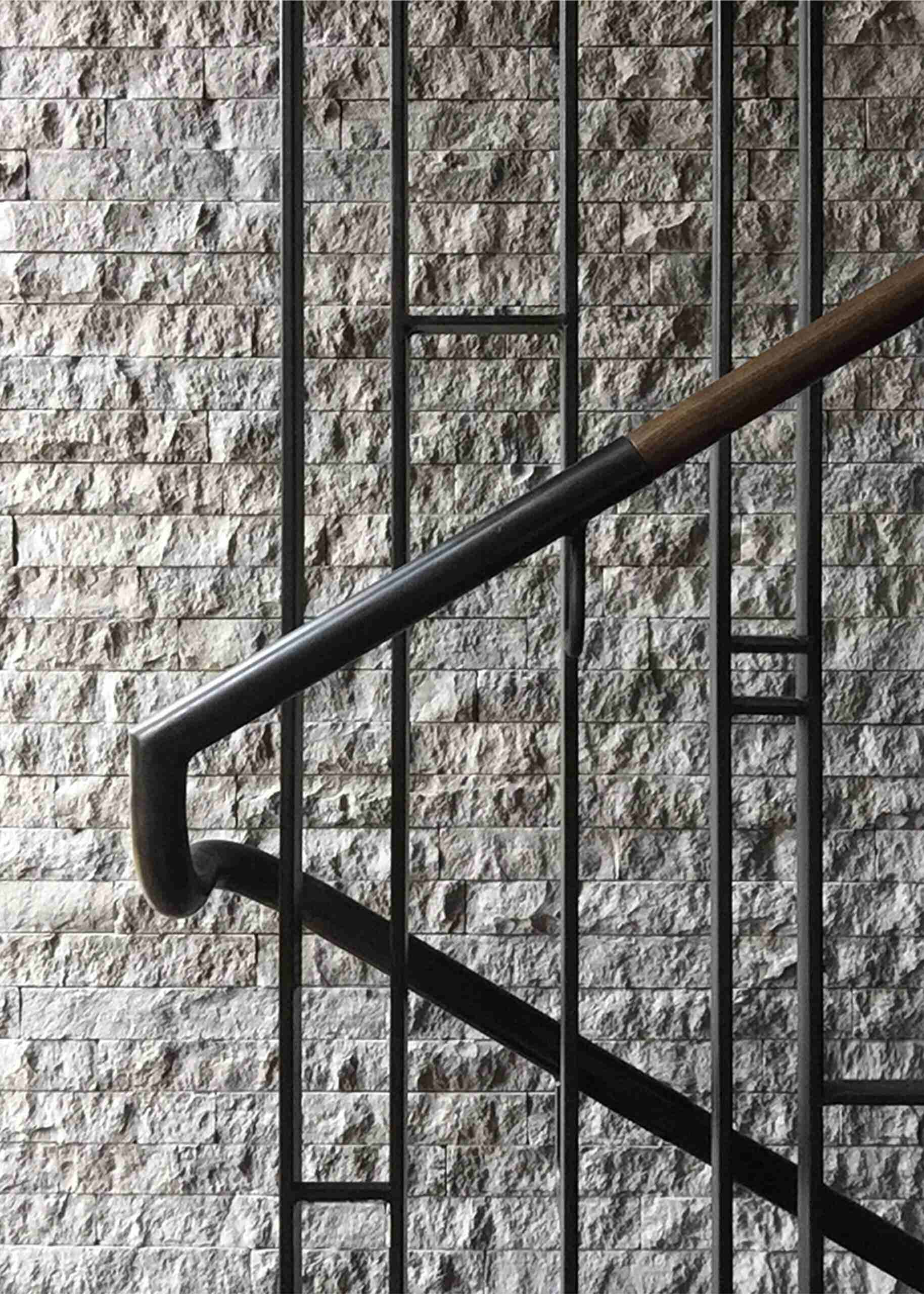 The stone wall from the living room continues along the staircase, creating a visual link between the levels. A light steel stair column was engineered to carry the structural load, doing away with heavy stringers and giving the stairs a floating effect.