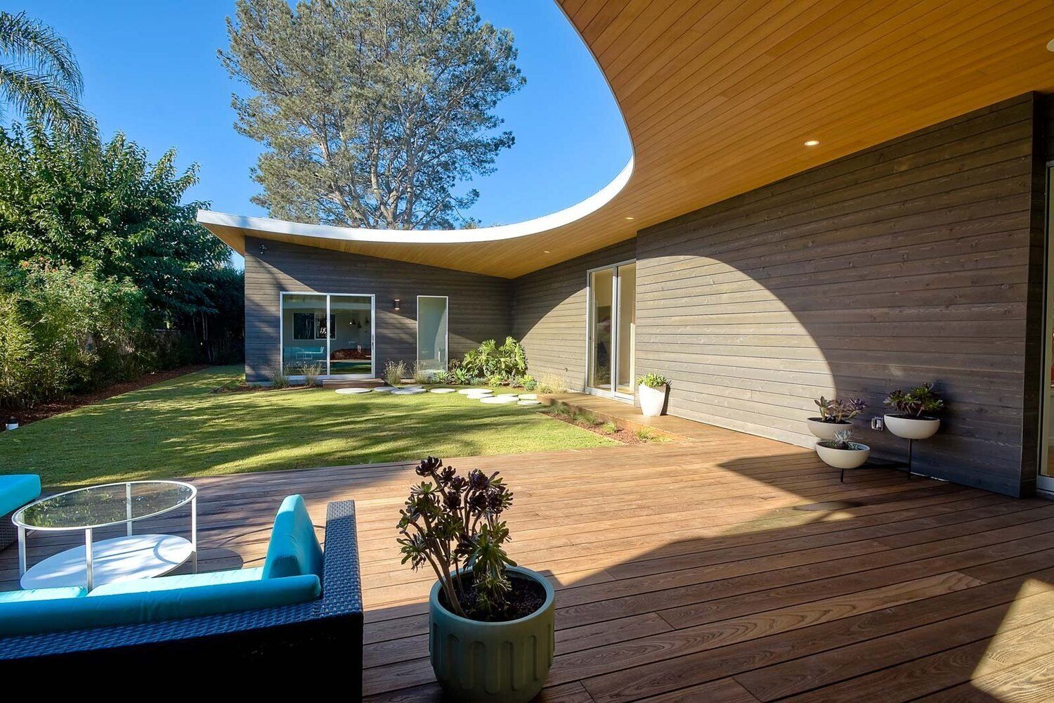 Curved roof with hidden lighting frames a wood patio furnished in bold blue.