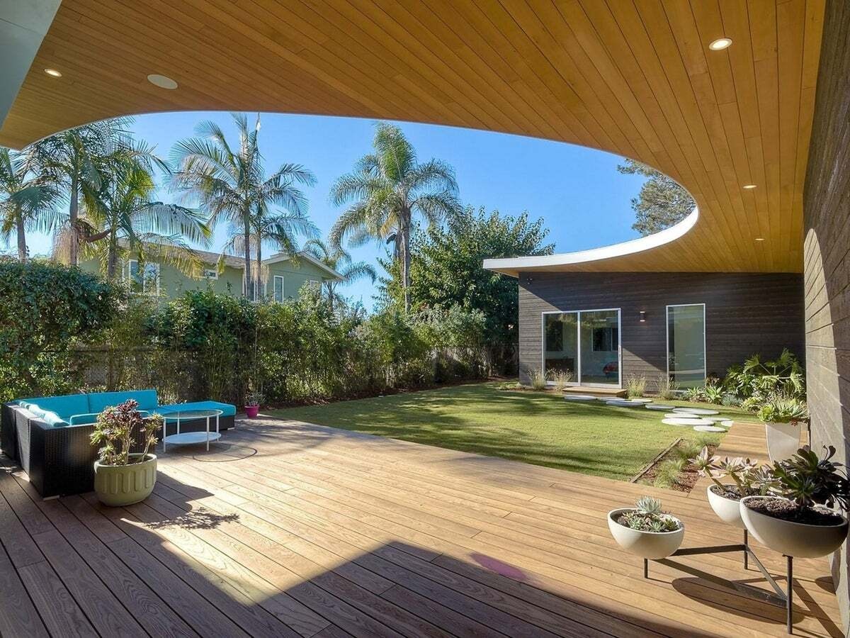 Curved roof with hidden lighting frames a wood patio furnished in bold blue.