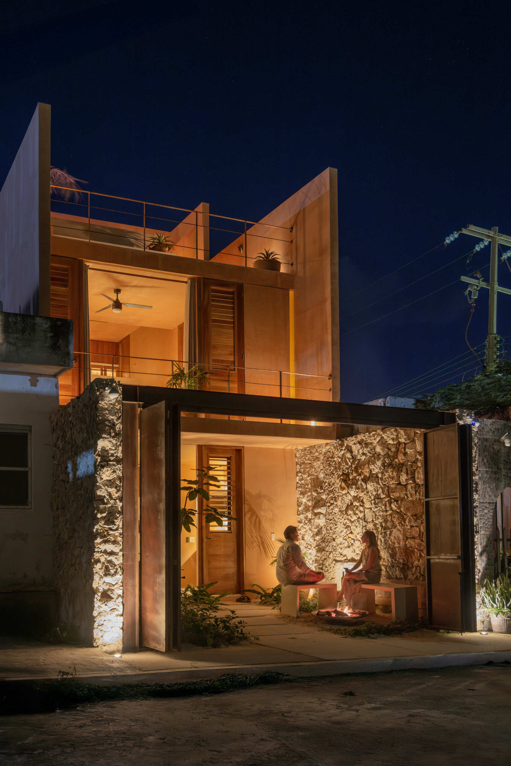 The lower unit features a garden, open kitchen, dining area, bedroom, and bathroom, designed to feel airy and connected through two sunlit courtyards.