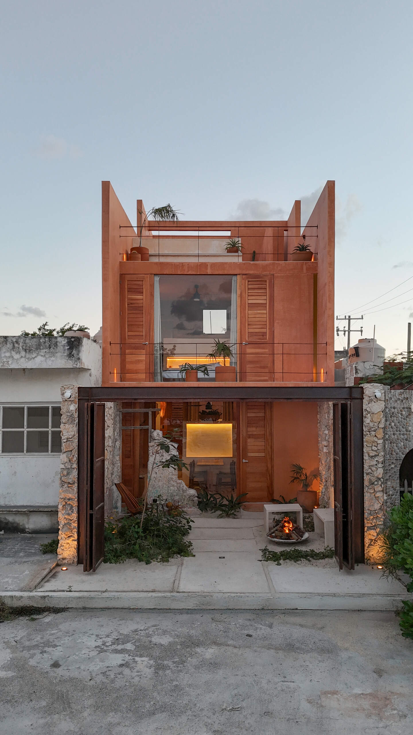 The lower unit features a garden, open kitchen, dining area, bedroom, and bathroom, designed to feel airy and connected through two sunlit courtyards.