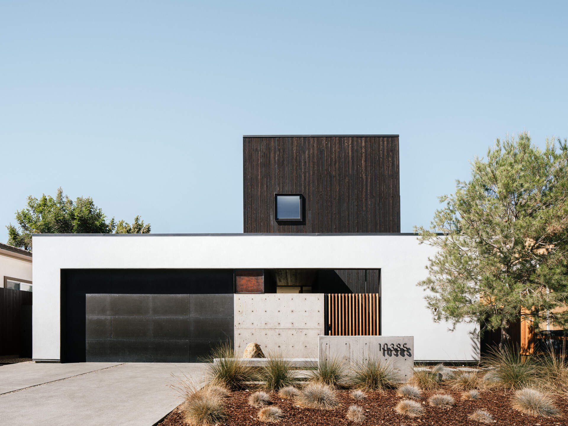 Stepped massing responds directly to strict zoning rules. From the street, white stucco walls echo surrounding houses, while the second level is clad in black shou sugi ban wood. 