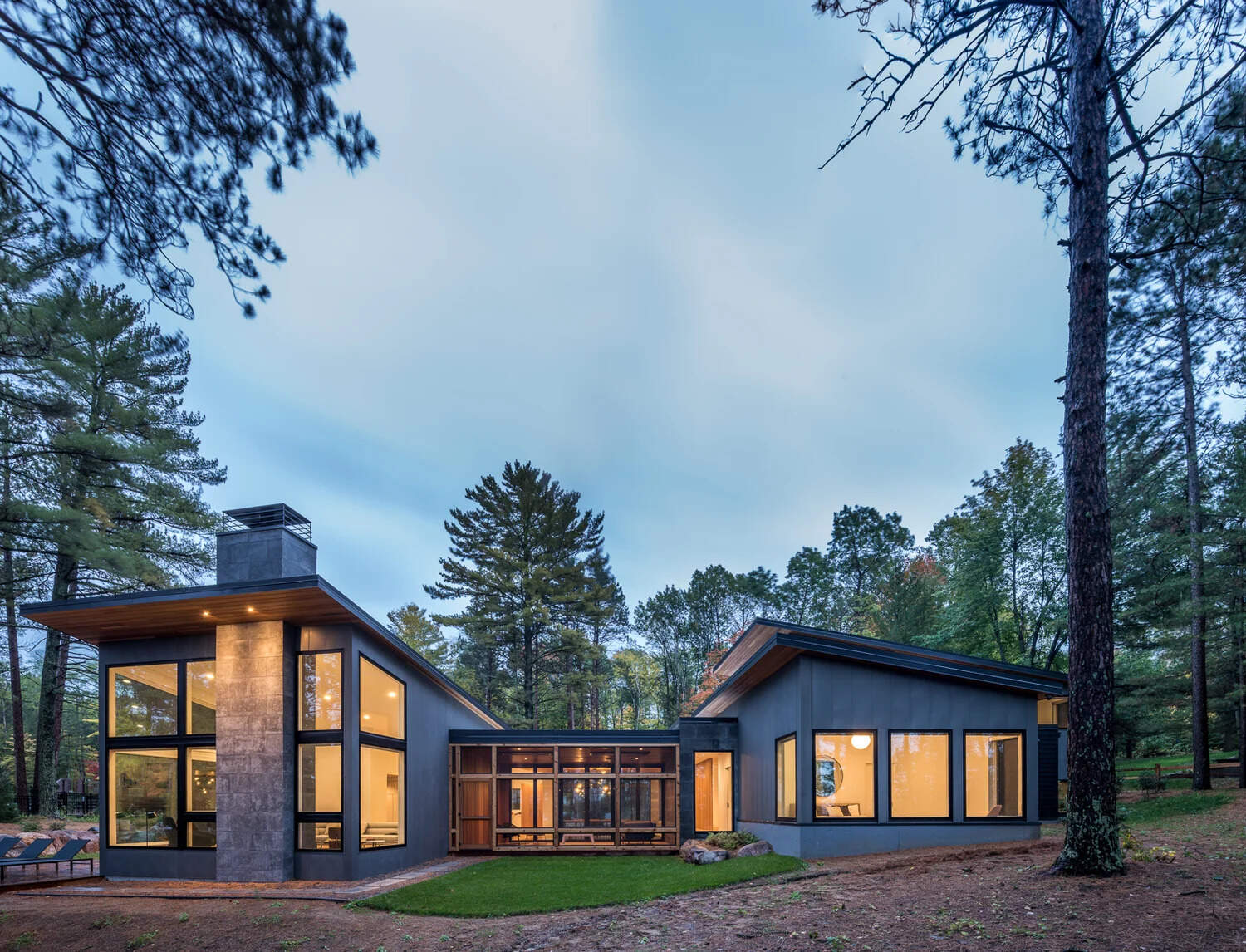 This modern house has a subtle dark exterior that includes grey, black, stone and wood elements, allowing the home to blend into the forested landscape.