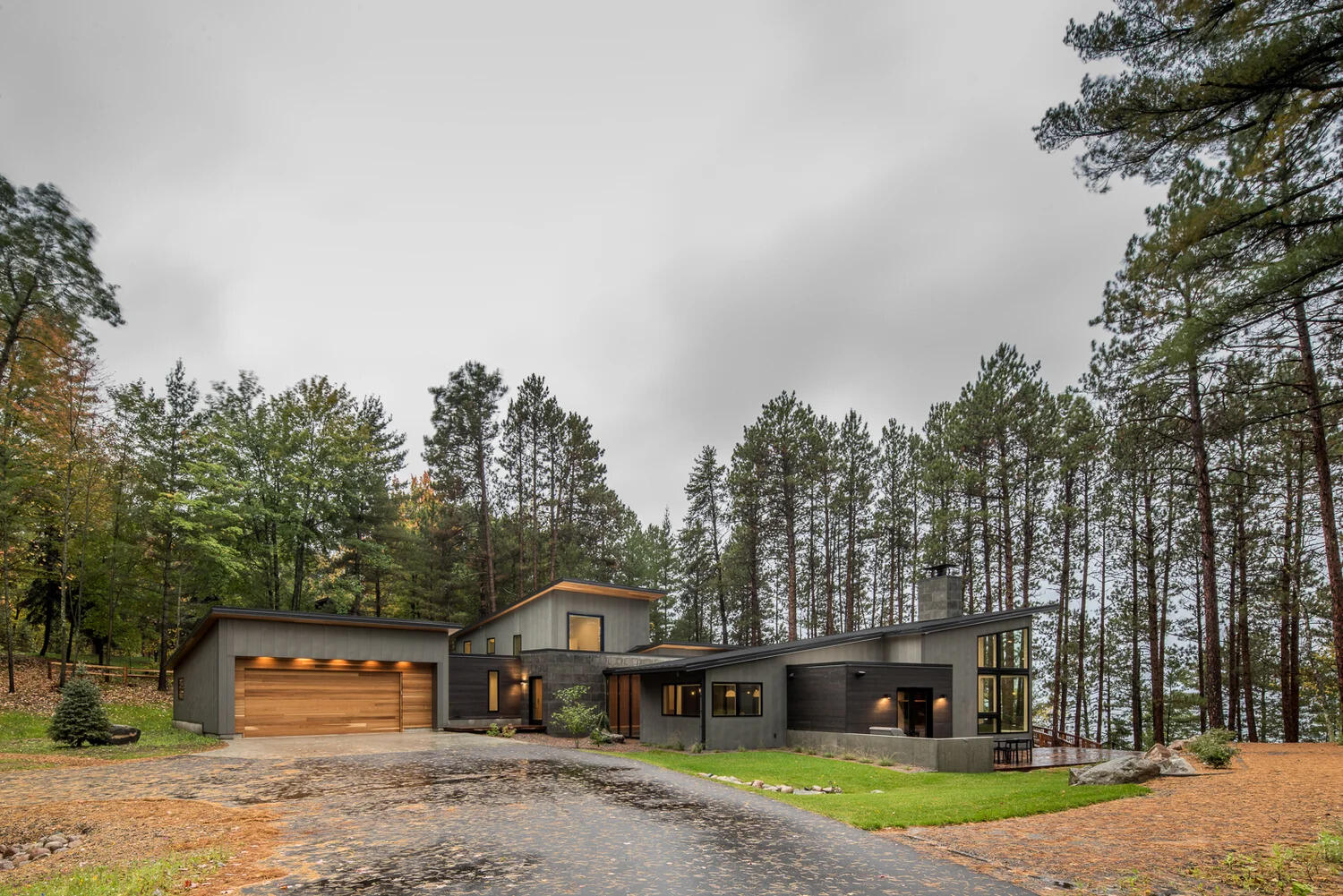 This modern house has a subtle dark exterior that includes grey, black, stone and wood elements, allowing the home to blend into the forested landscape.