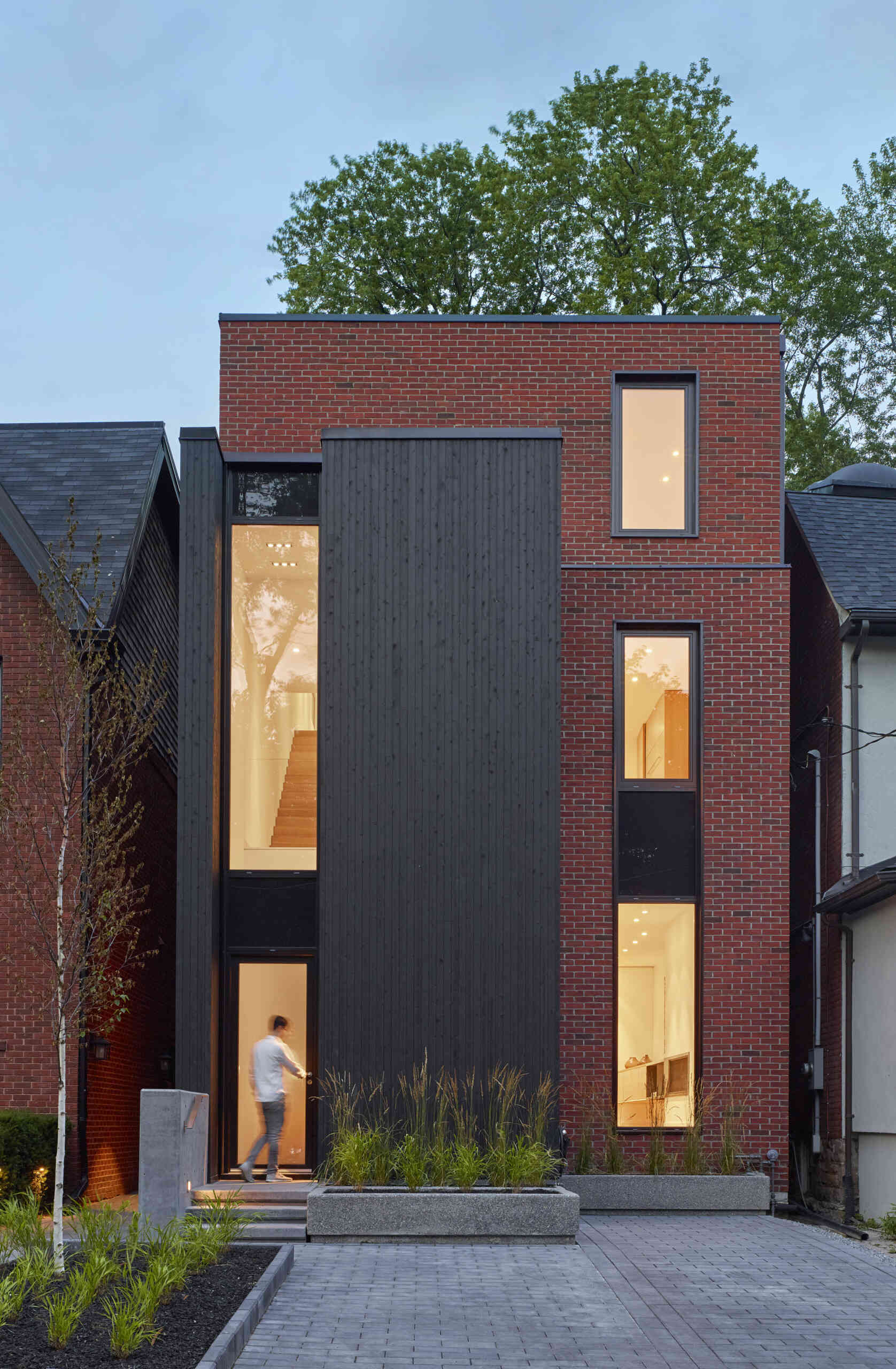 A striking modern home in Toronto’s Summerhill neighborhood by Akb Architects, featuring bold red brick, black-stained cedar, and tall narrow windows that give the facade a graphic, architectural rhythm.