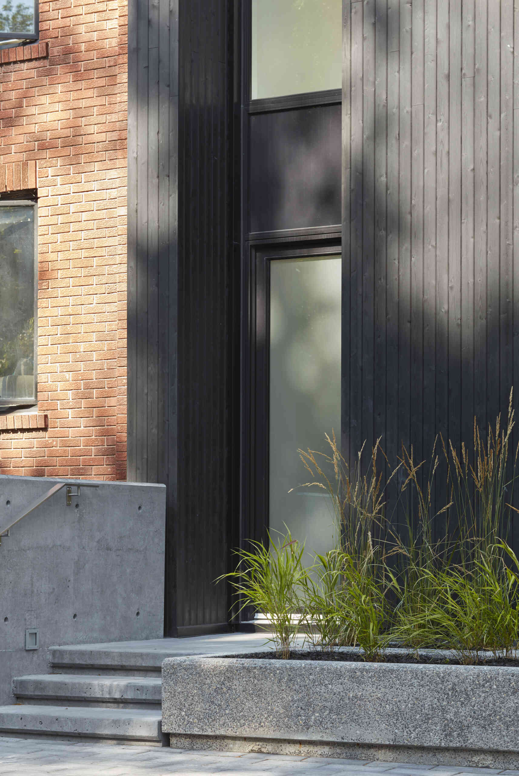 A striking modern home in Toronto’s Summerhill neighborhood by Akb Architects, featuring bold red brick, black-stained cedar, and tall narrow windows that give the facade a graphic, architectural rhythm.