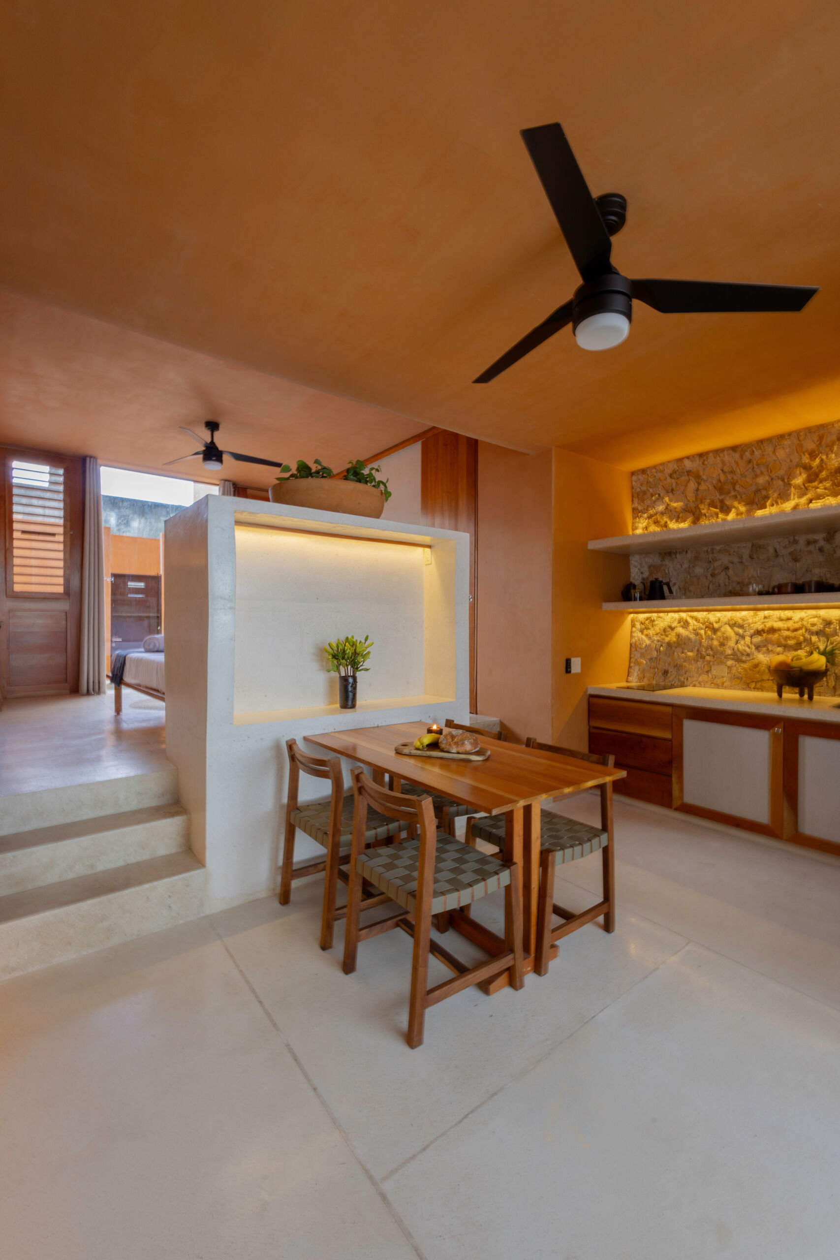The lower unit features a garden, open kitchen, dining area, bedroom, and bathroom, designed to feel airy and connected through two sunlit courtyards.