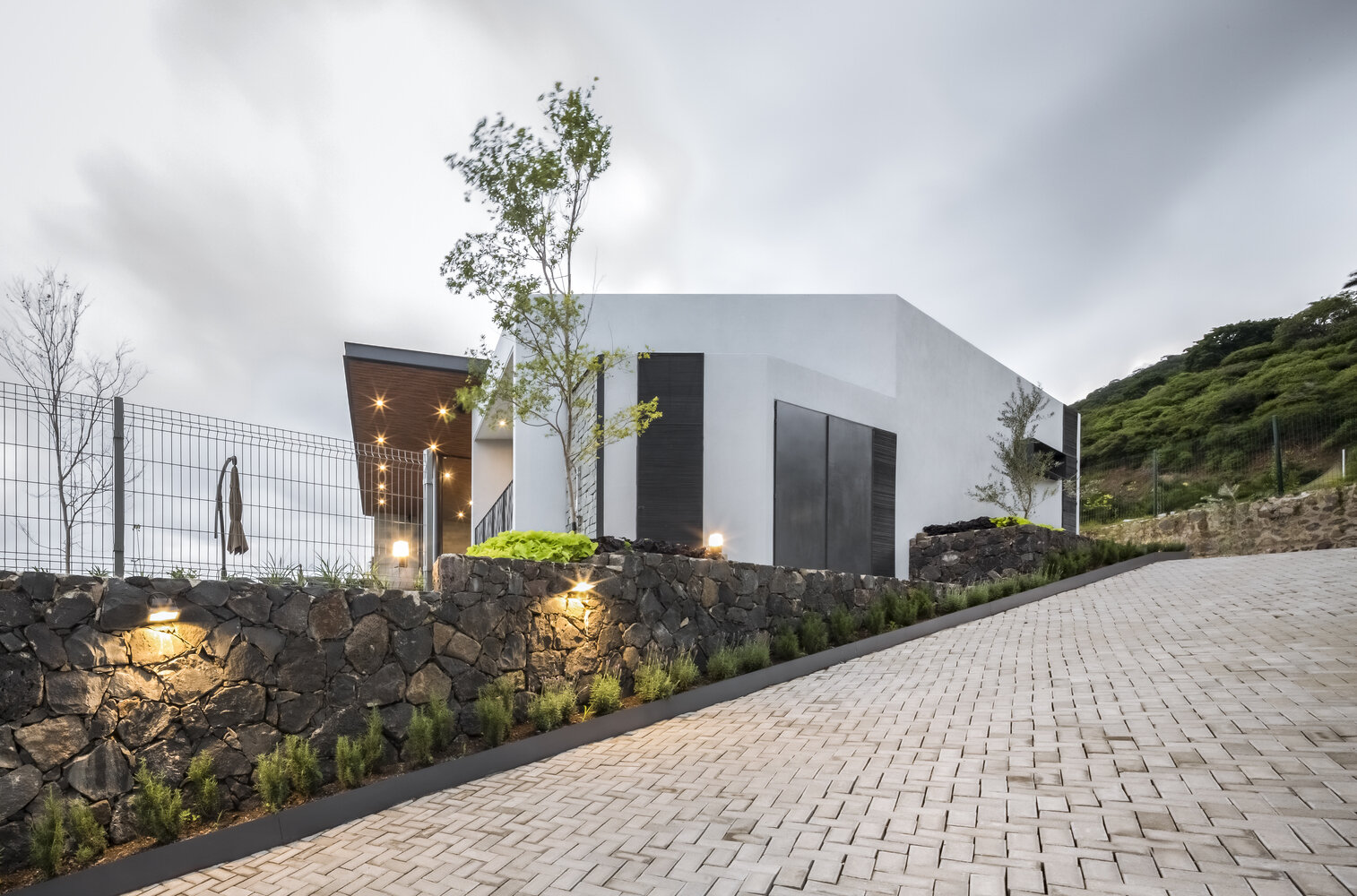 A textured stone wall guides visitors toward the entry, anchoring the home to its lakeside hillside setting.